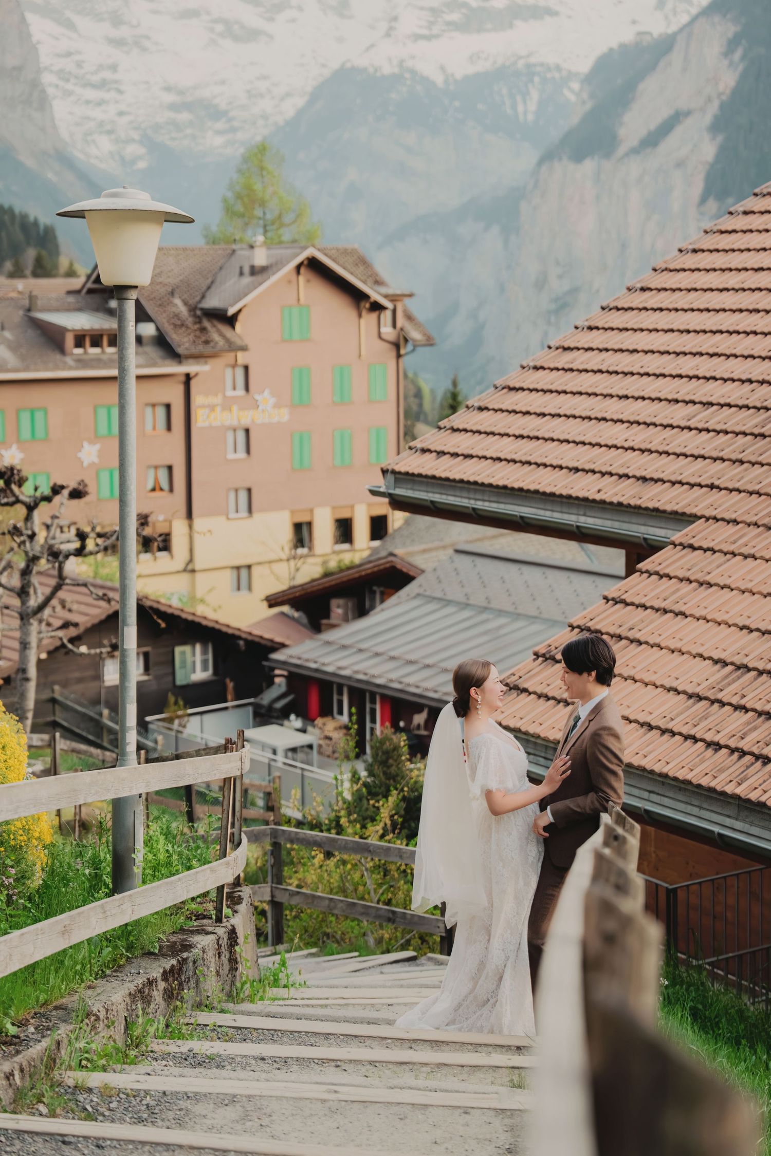 Elegant bride and groom embracing on rustic wooden staircase in a picturesque Swiss mountain village setting.
