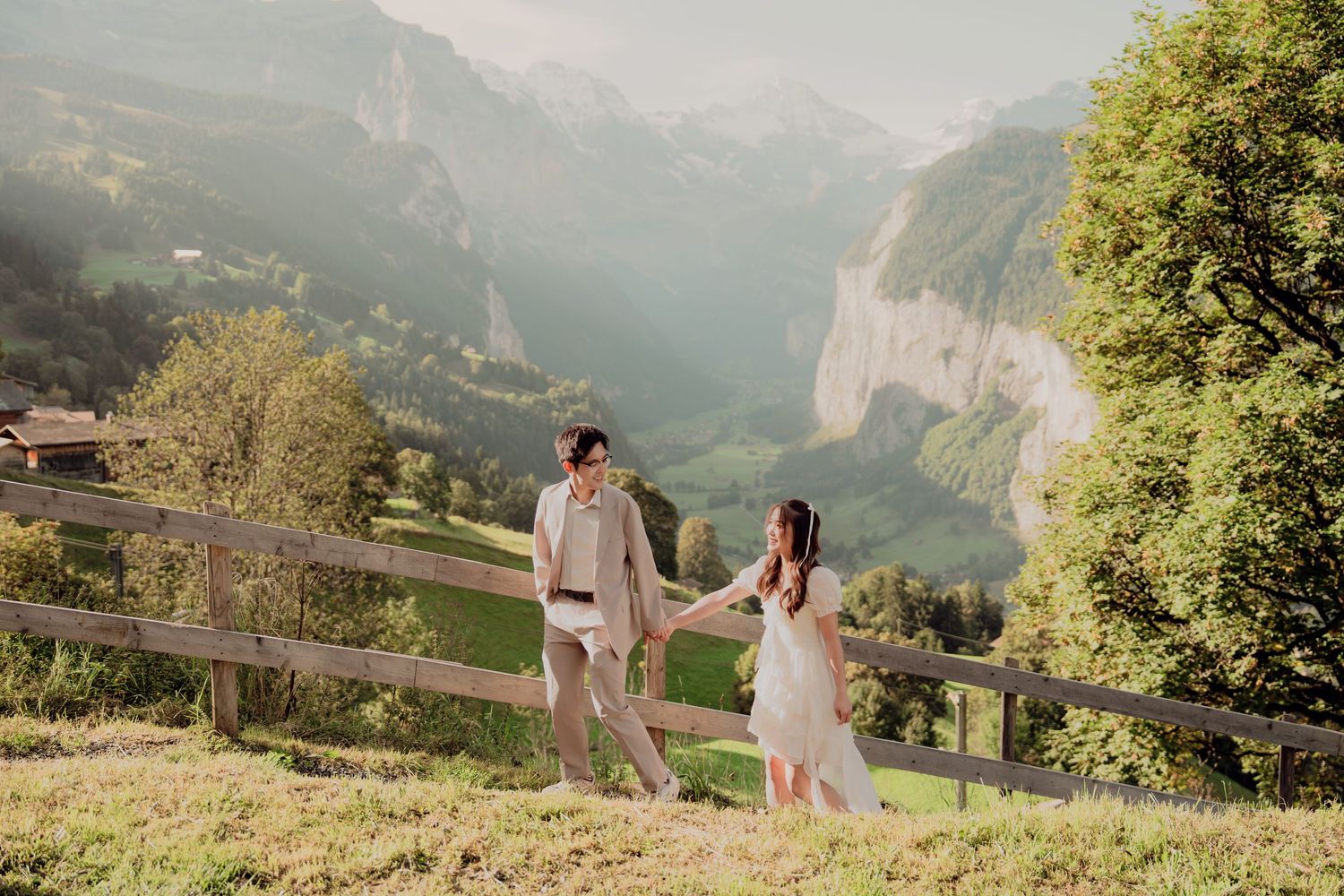 Bride and groom holding hands by a rustic fence with breathtaking Lauterbrunnen valley views.