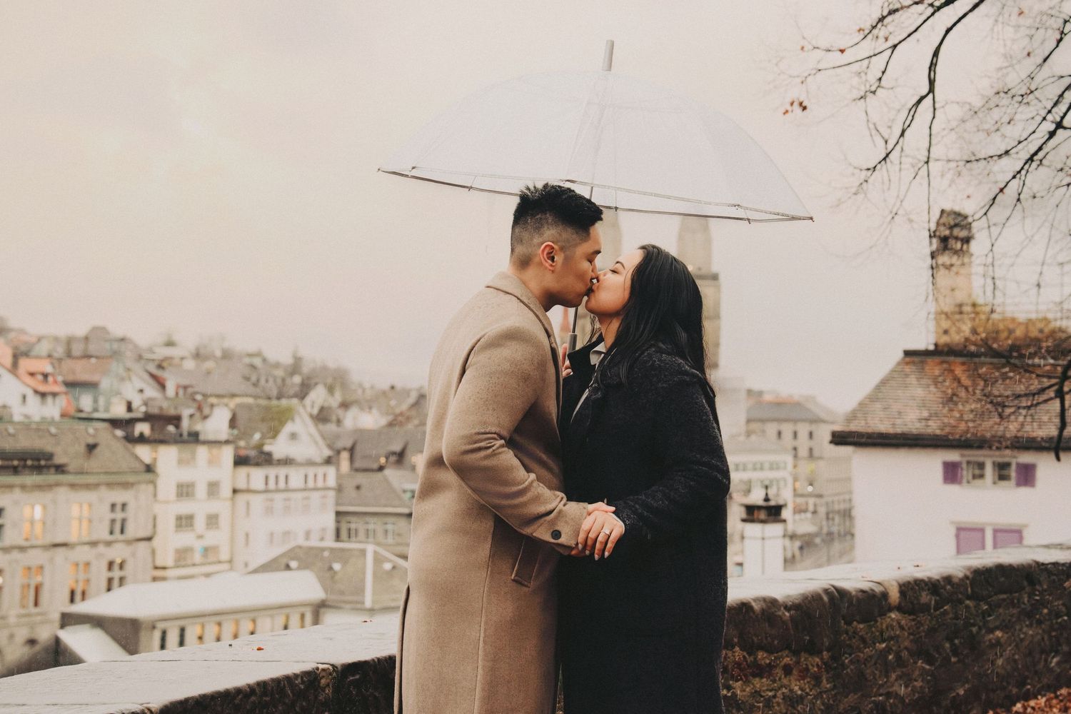 Couple kissing under a transparent umbrella with the historic Zurich cityscape in the background.