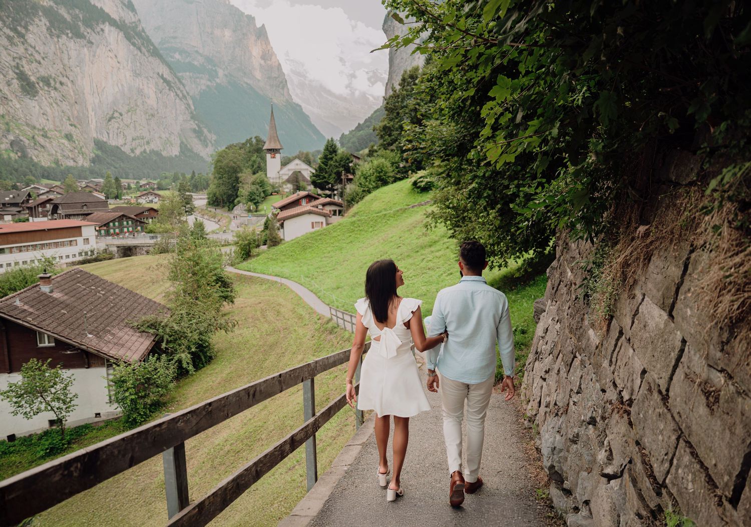 Newly engaged couple walks hand in hand along a scenic path in a Swiss mountain village.