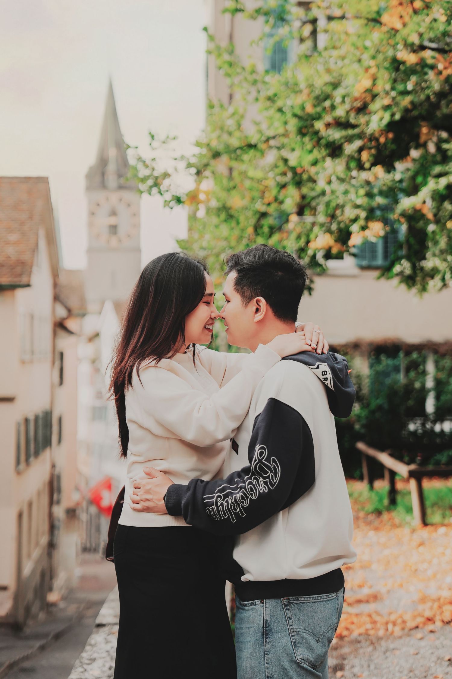 Couple embracing and smiling at each other on a cobblestone street in Zurich's old town with church tower backdrop.