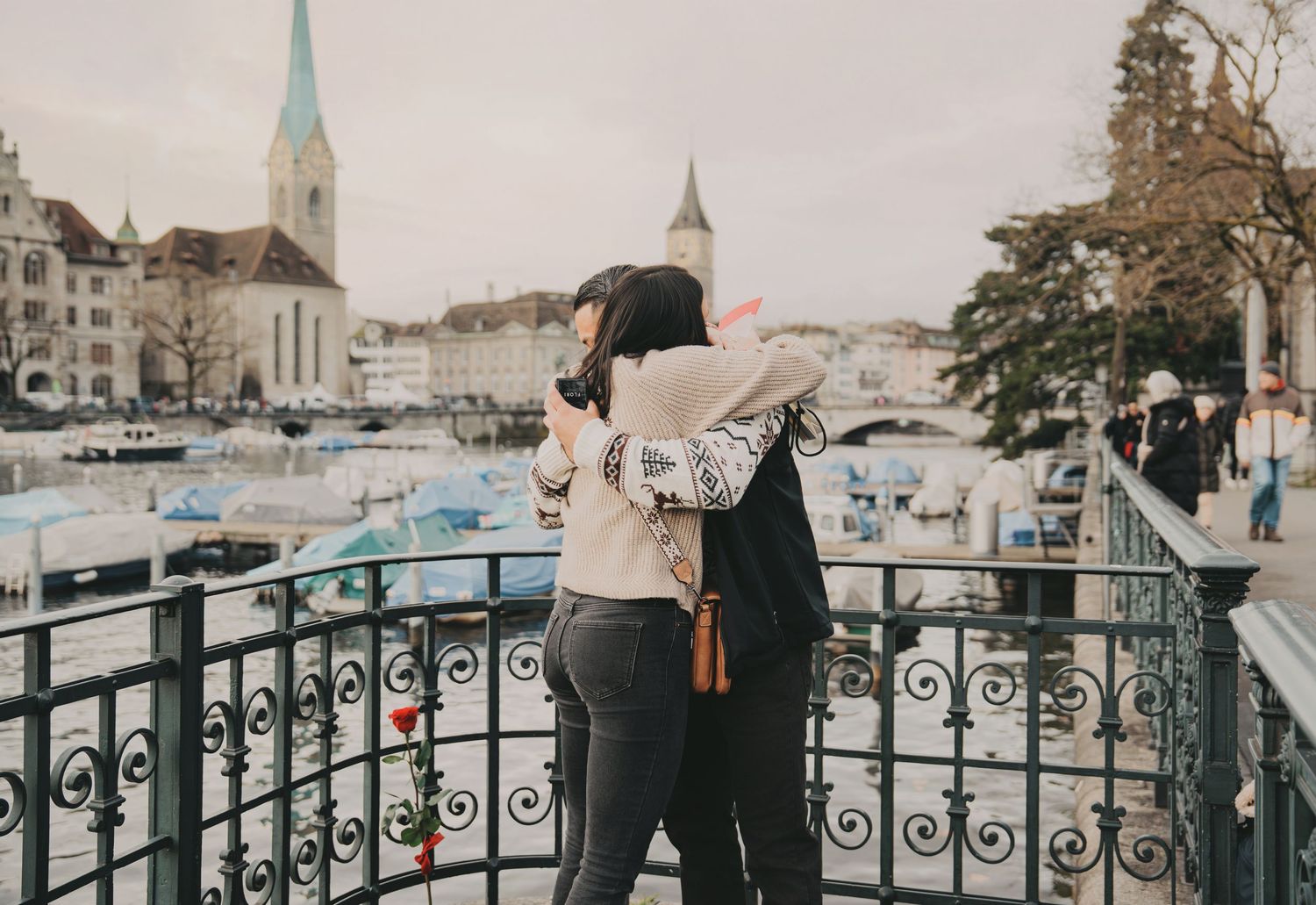 Couple embracing on decorative iron bridge with Zurich old town and harbor in background.