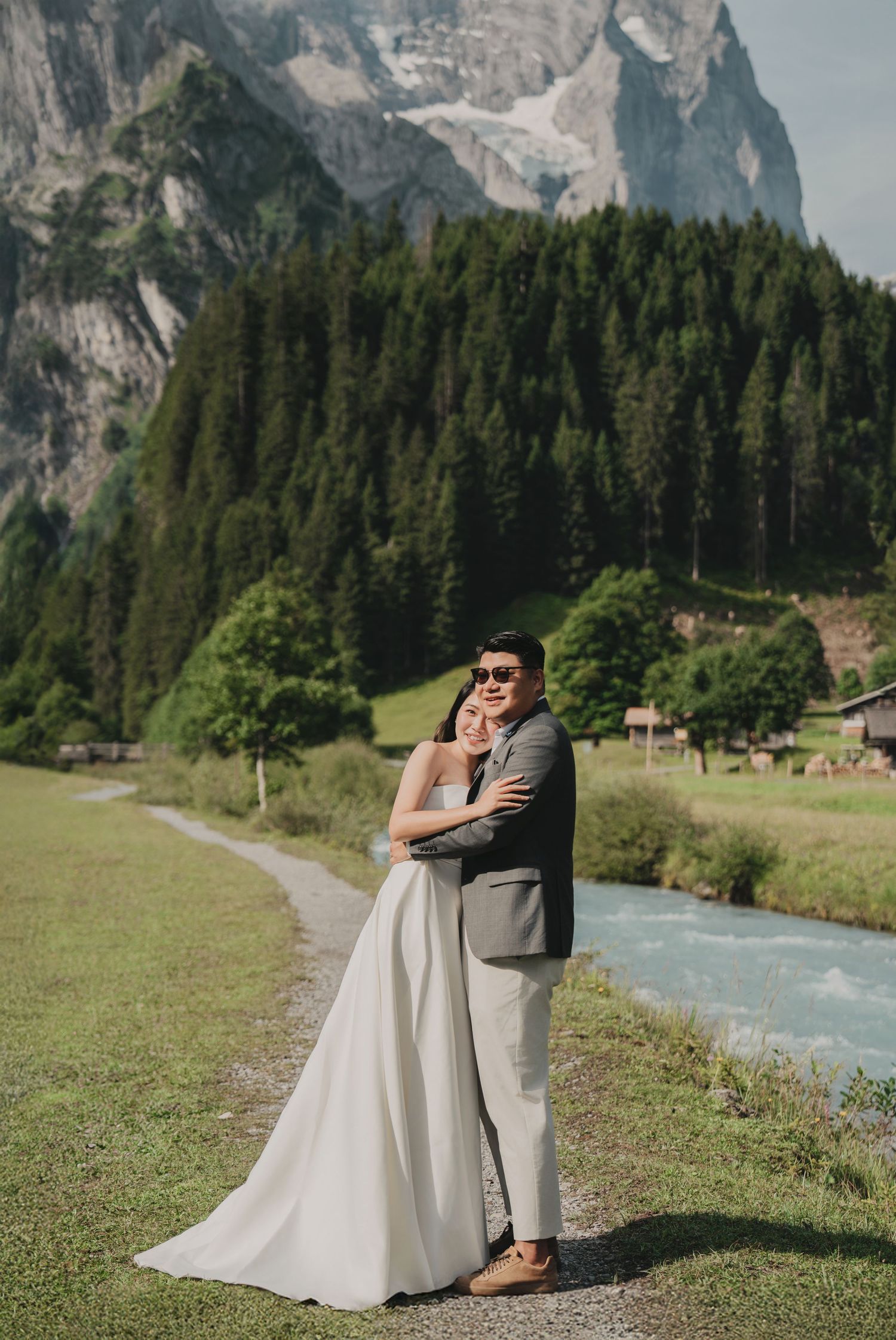 Bride and groom posing together beside a turquoise river with dramatic Swiss mountain backdrop.