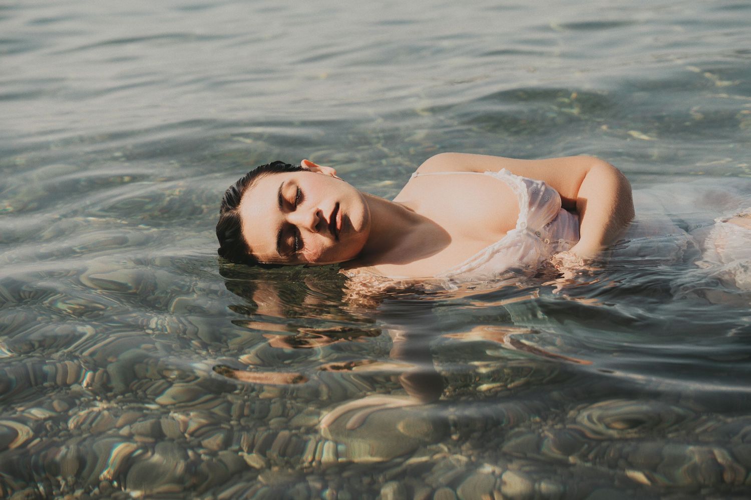 Young woman in white swimsuit floating peacefully on her back in clear shallow sea water.