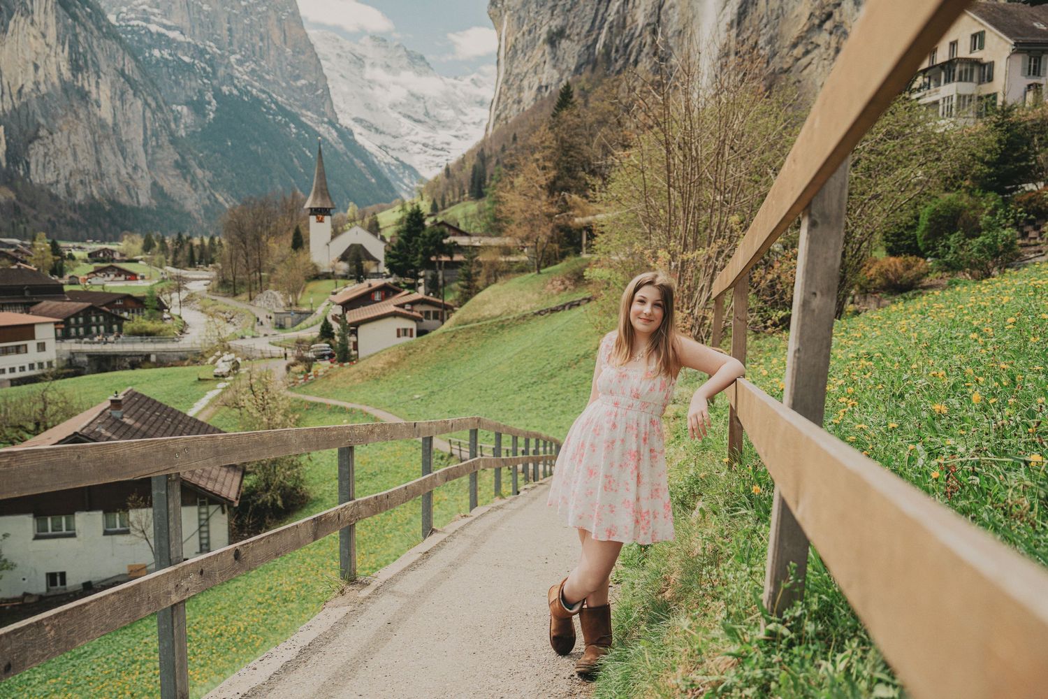 Young girl in a pink floral dress posing on a scenic mountain path in a Swiss alpine village.