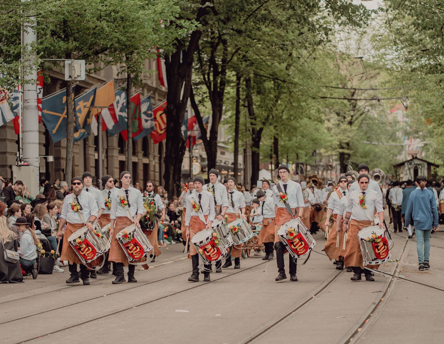 Marching band in traditional costumes playing drums along a tree-lined street.