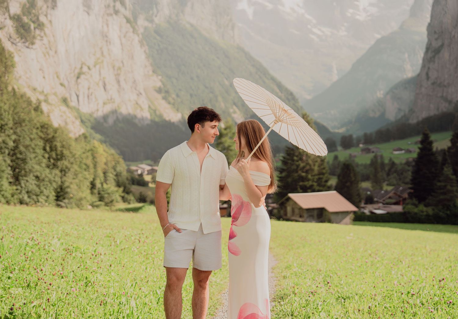 Couple standing in a lush green alpine meadow with dramatic Swiss mountain cliffs and a parasol in Lauterbrunnen.