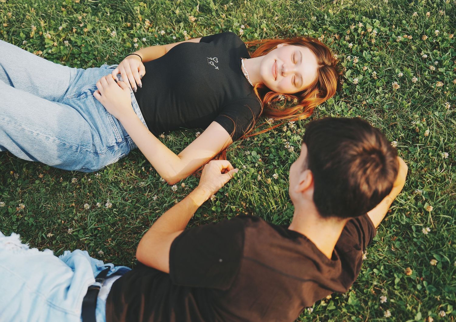 Aerial view of couple lying on grass holding hands, woman with auburn hair smiling warmly.