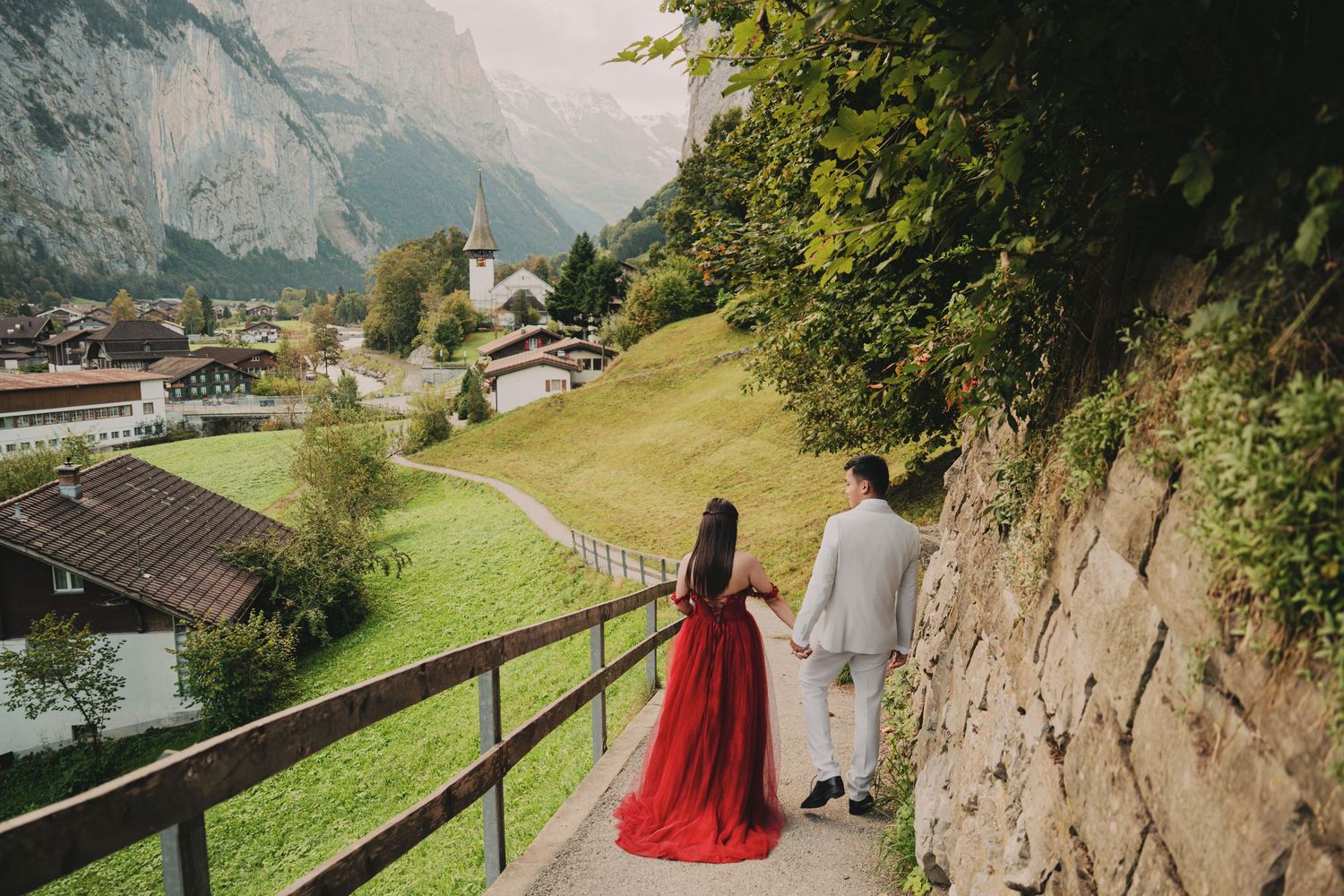 Romantic couple walking hand in hand on scenic Swiss mountain village pathway with church view.