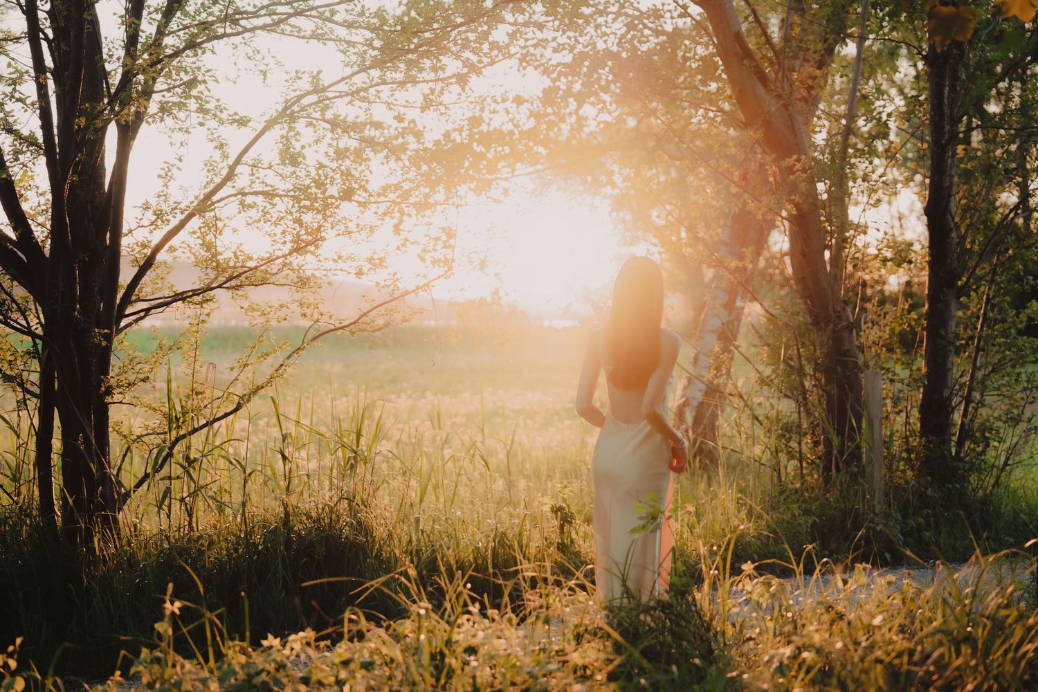 Woman in white dress standing in golden sunset light in forest.