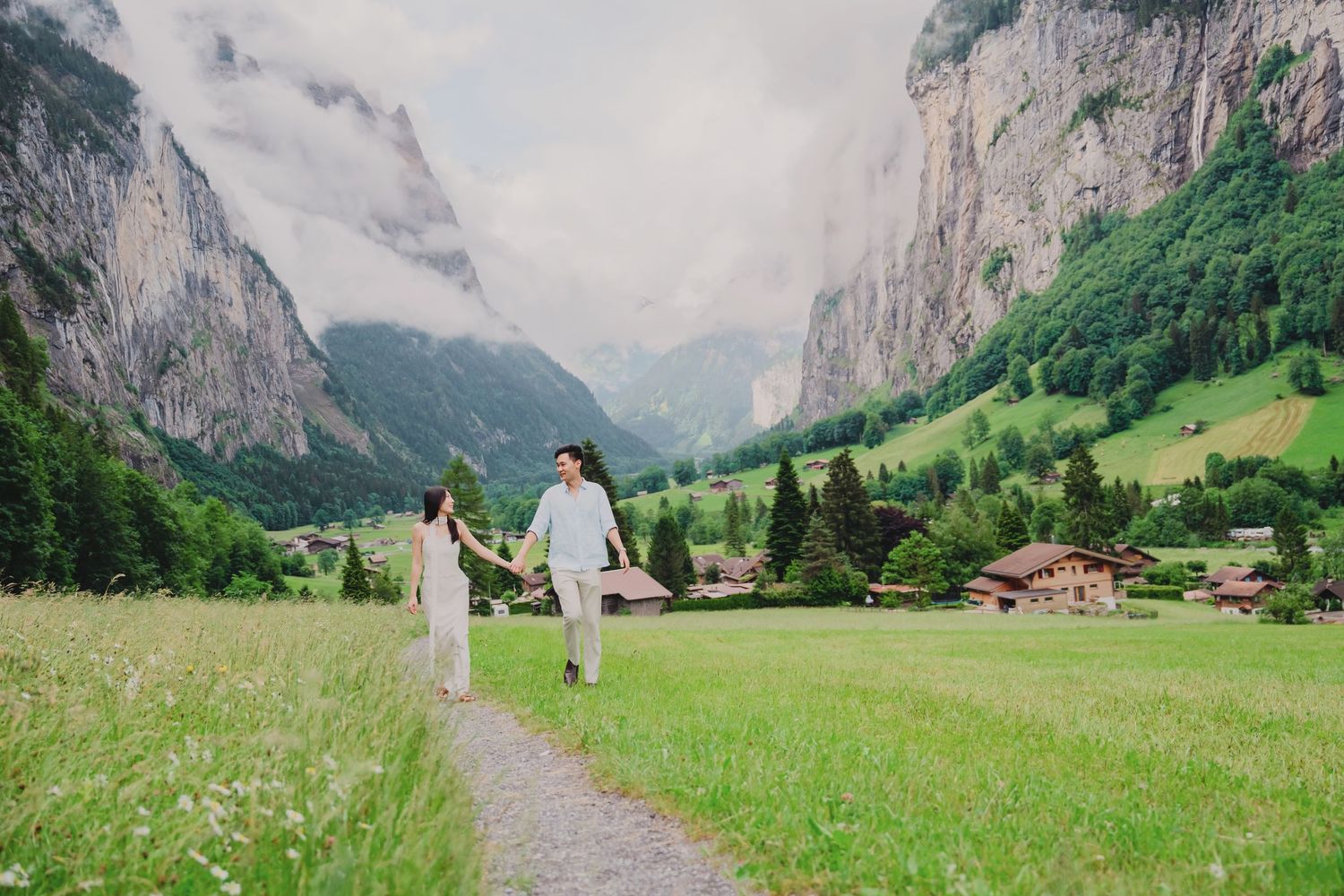 Couple holding hands walking along a path through a lush green valley surrounded by mountains in Lauterbrunnen, Switzerland.