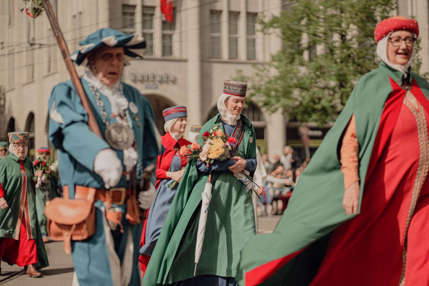 Colorful medieval costume parade with participants in green and red cloaks at a street festival.