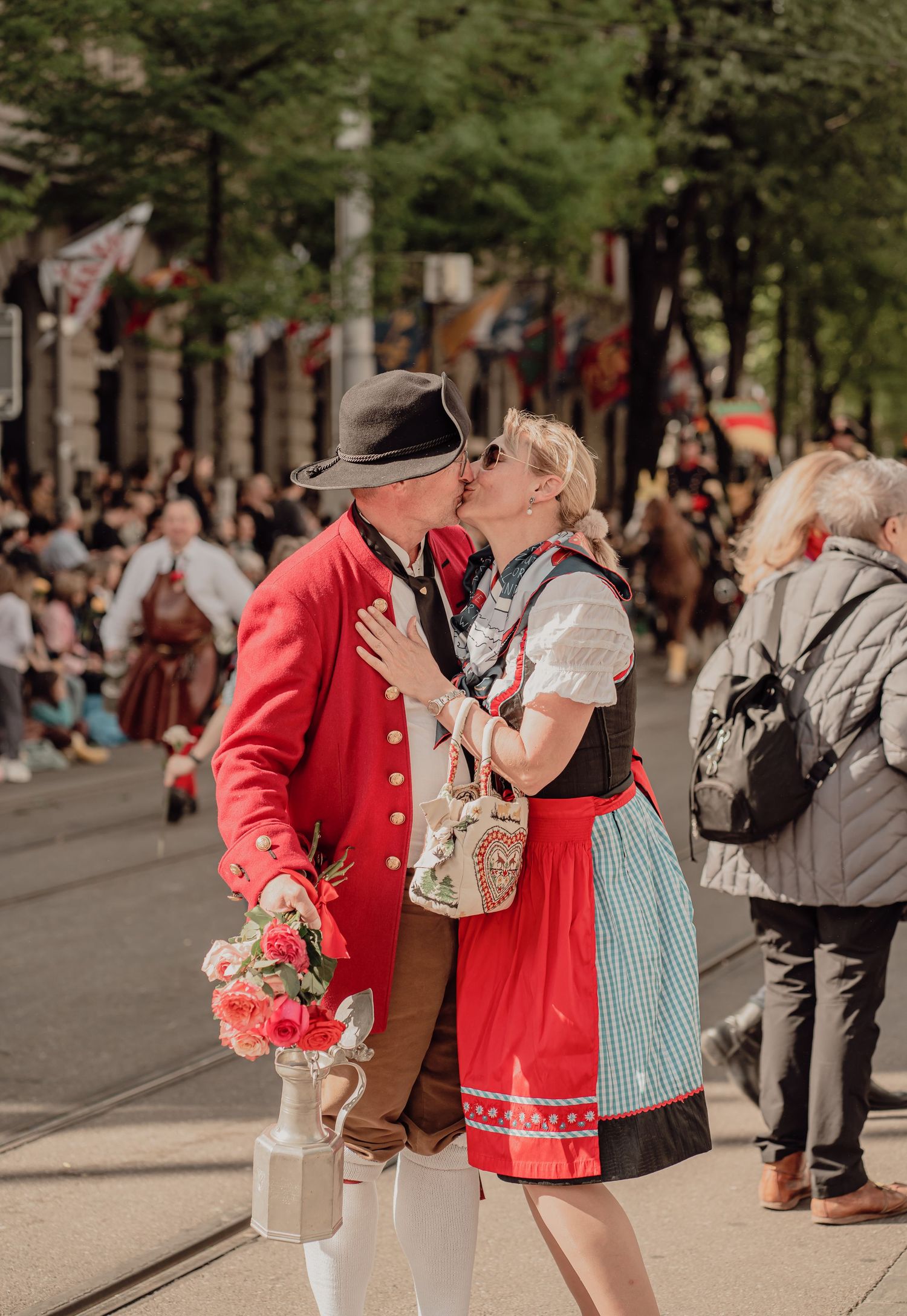 Couple in traditional Bavarian attire share a kiss during a colorful historical street festival.