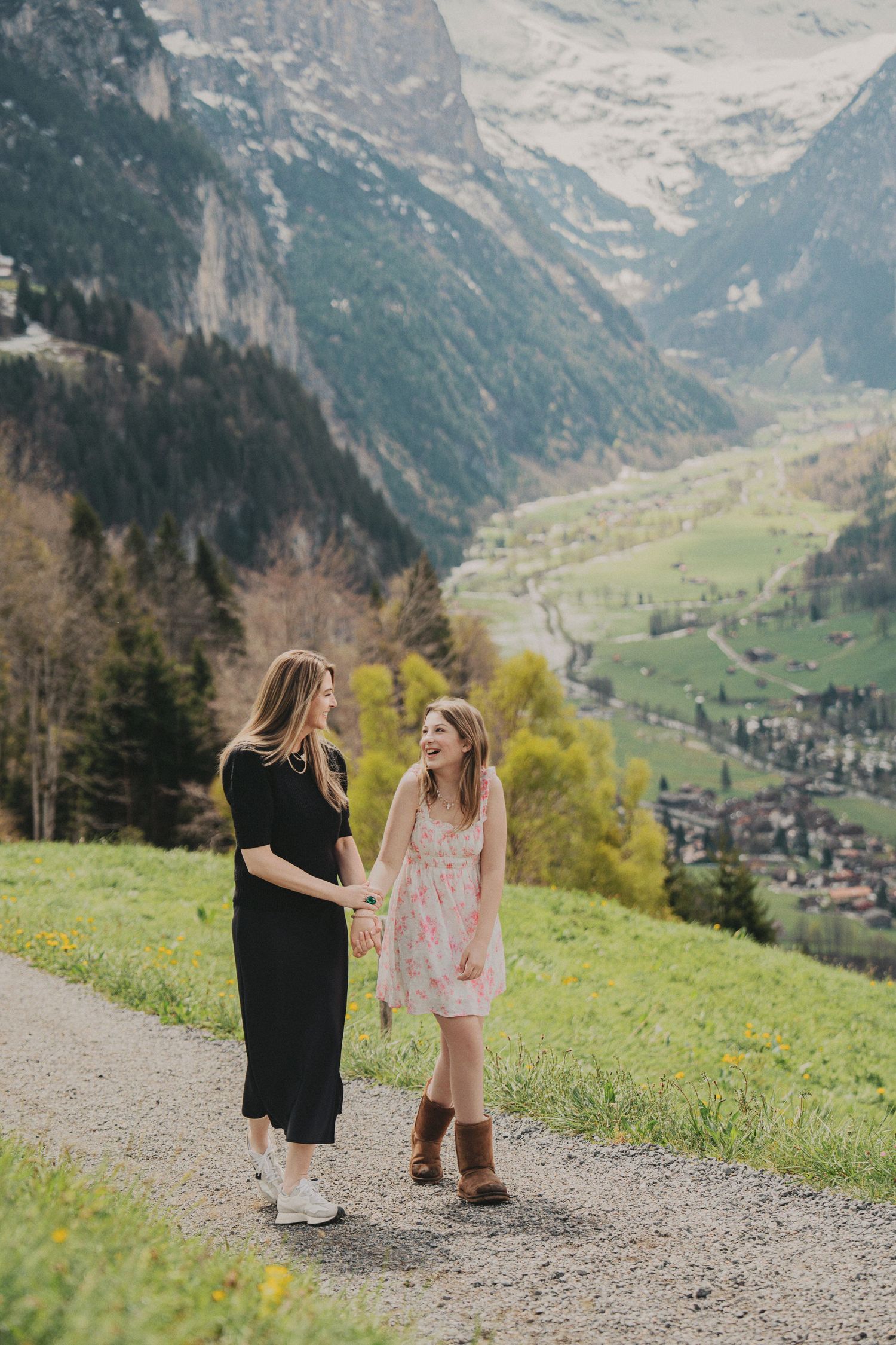 Mother and daughter holding hands and laughing on a scenic Swiss Alpine mountain path.