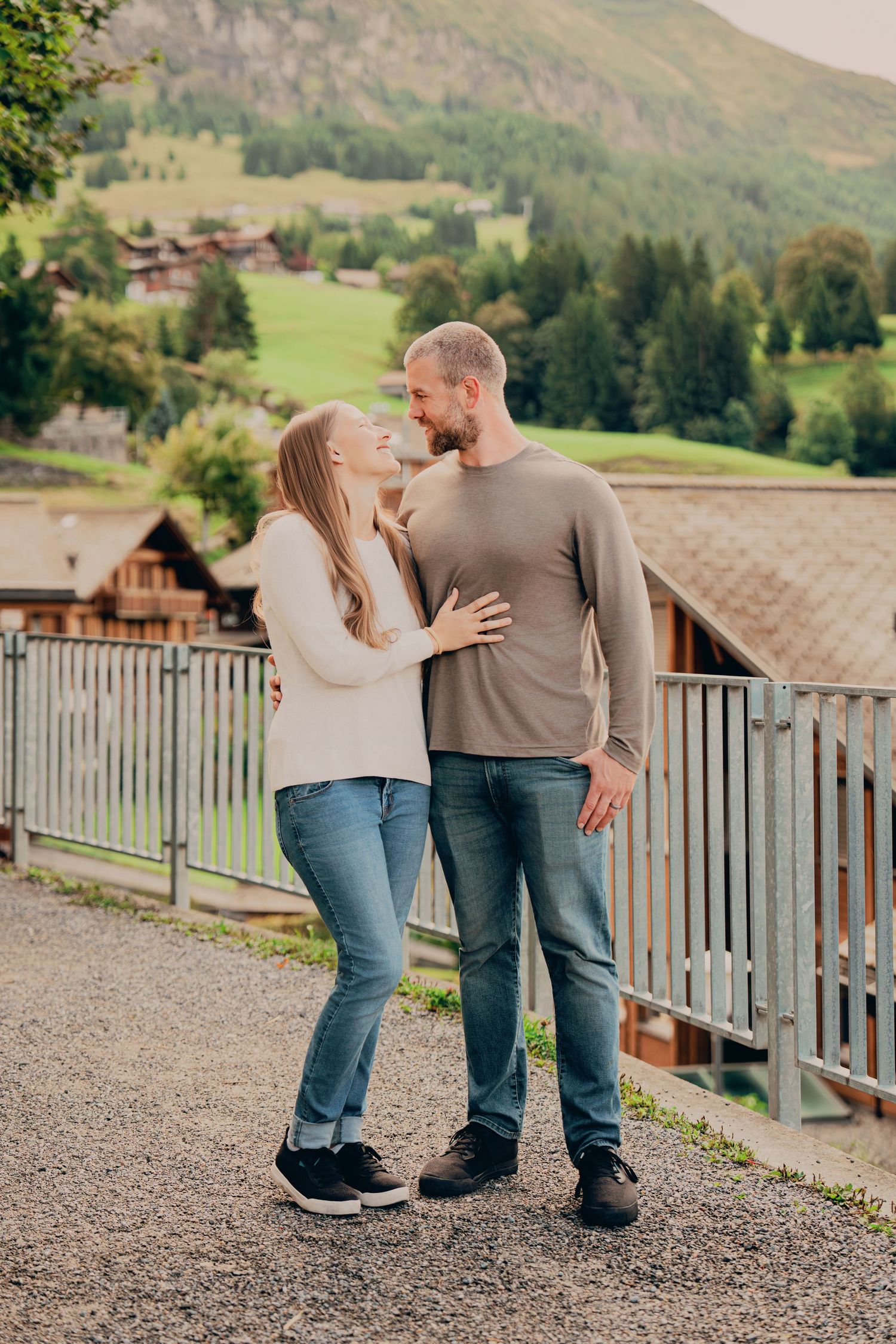 A loving couple gazes at each other on a gravel path with lush Swiss mountain scenery.