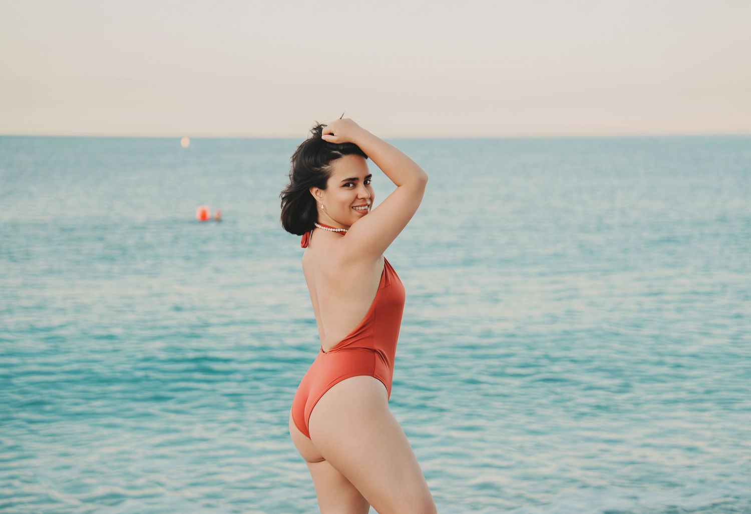 Woman in red swimsuit posing by the ocean at sunset on beach.