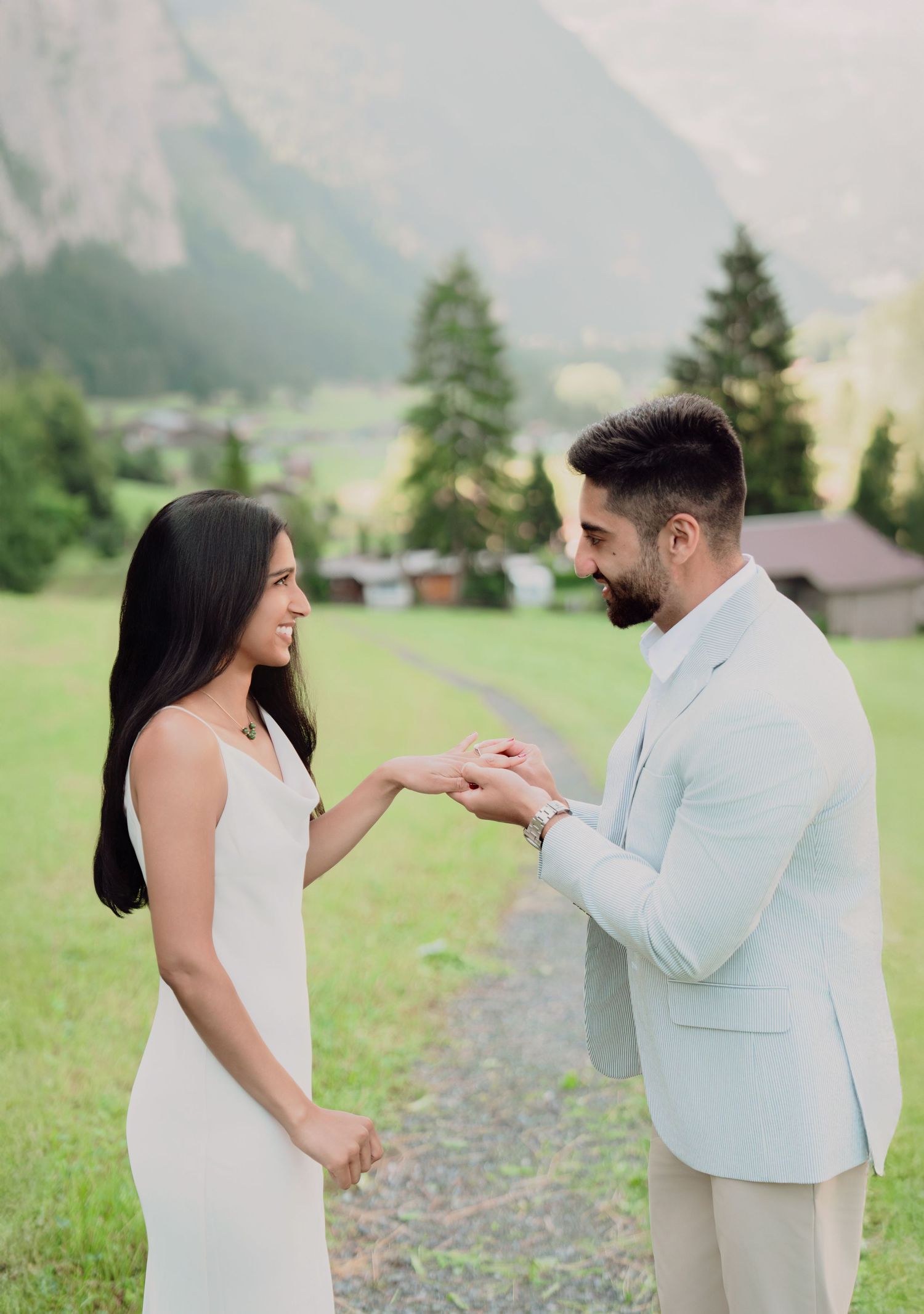 Couple sharing a joyful engagement moment holding hands in a lush green Swiss mountain valley.