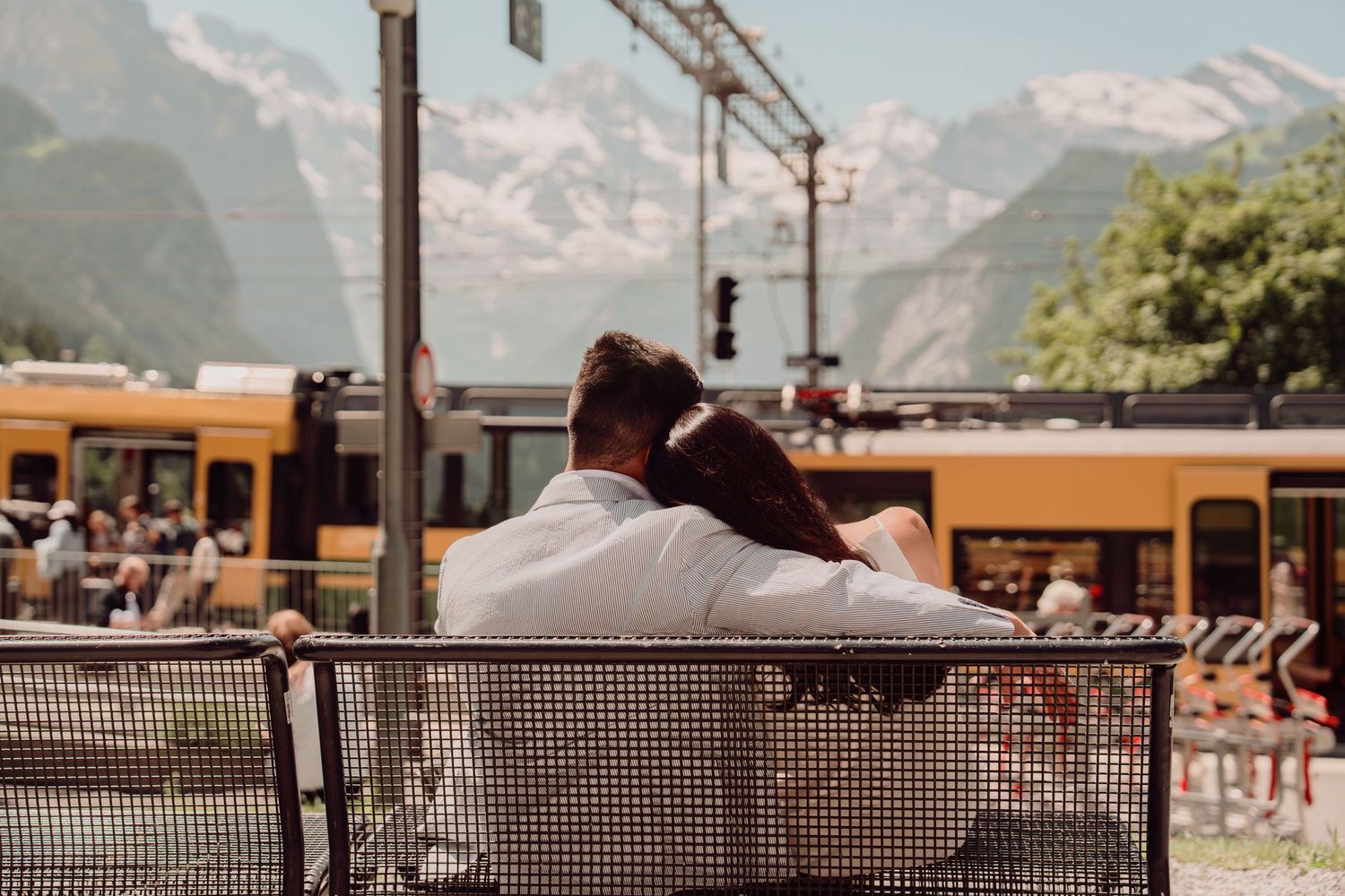 Couple cuddling on a bench from behind with Swiss mountain railway and Alps in the background.