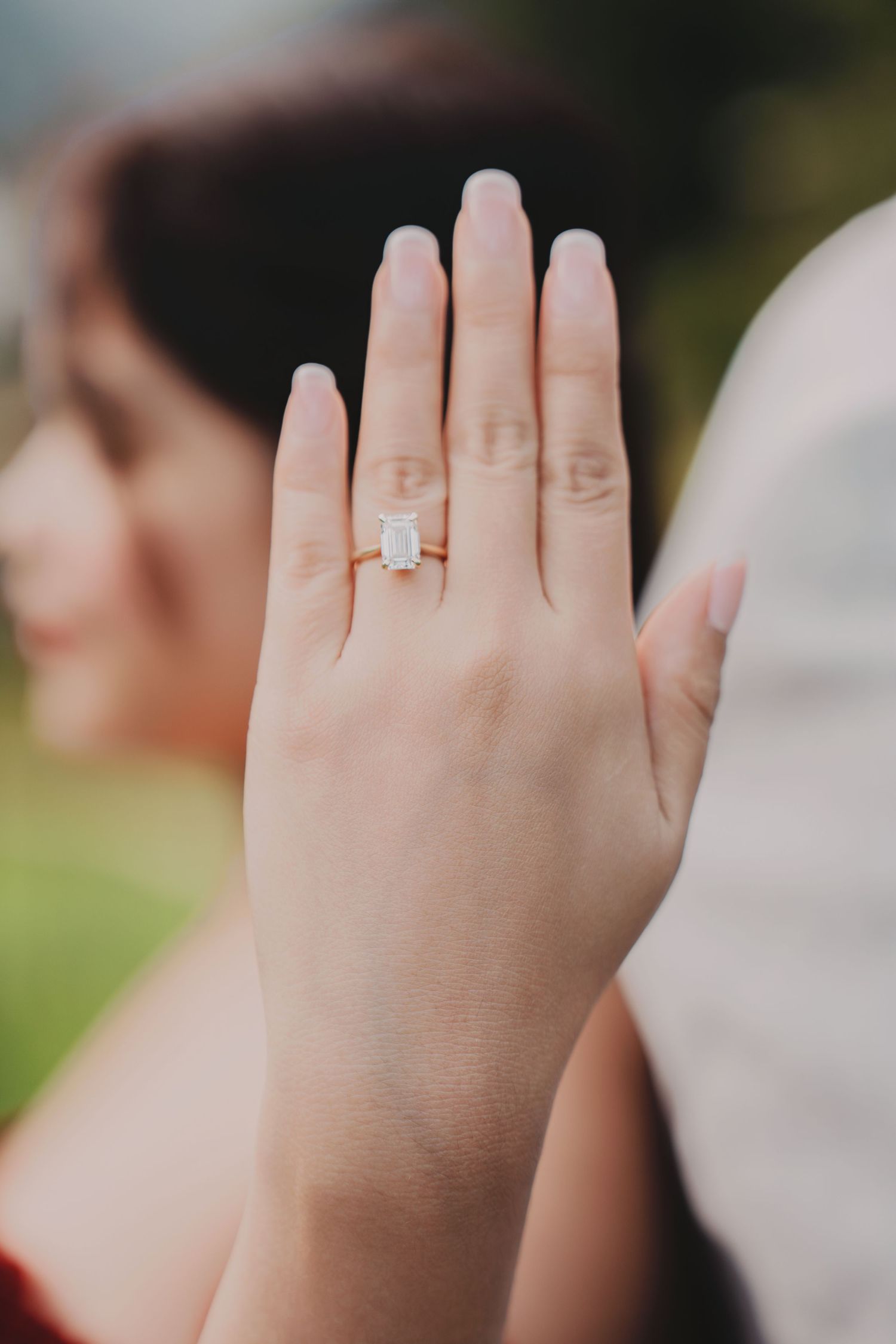Close-up of elegant emerald-cut diamond engagement ring on rose gold band on bride's hand.