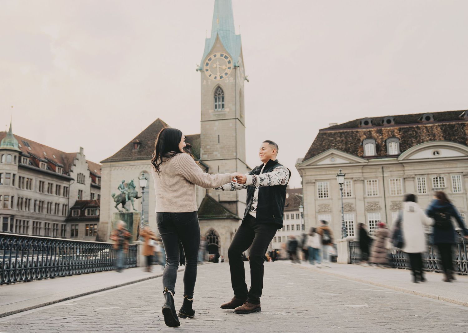 Romantic couple dancing on Munsterbrucke bridge in Zurich with blurred crowd background.