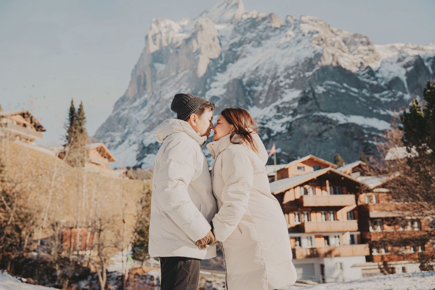 Romantic couple holding hands facing each other with Swiss alpine mountain scenery in winter.