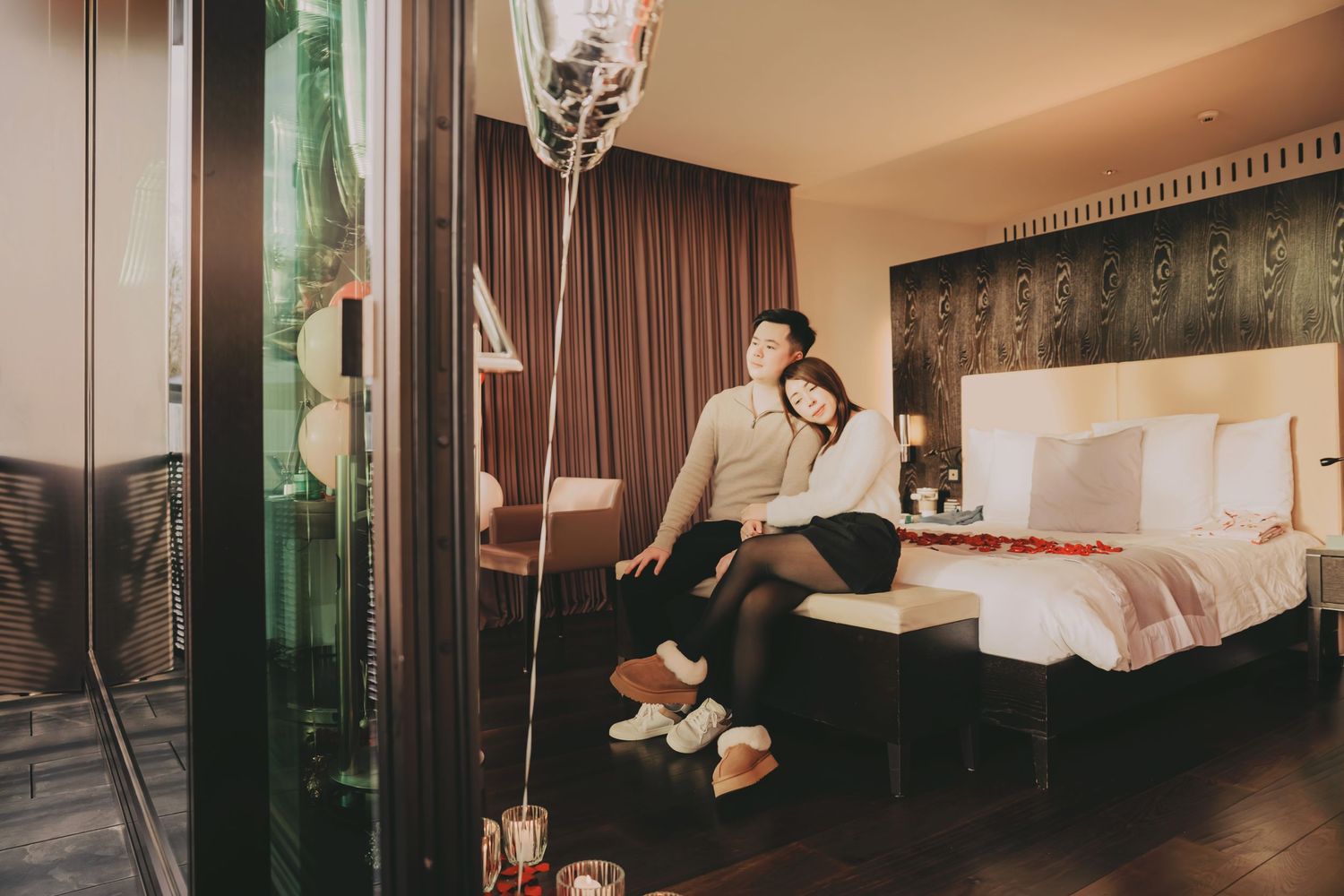 Couple relaxing together in a beautifully decorated hotel room with balloons and rose petals for a romantic occasion.