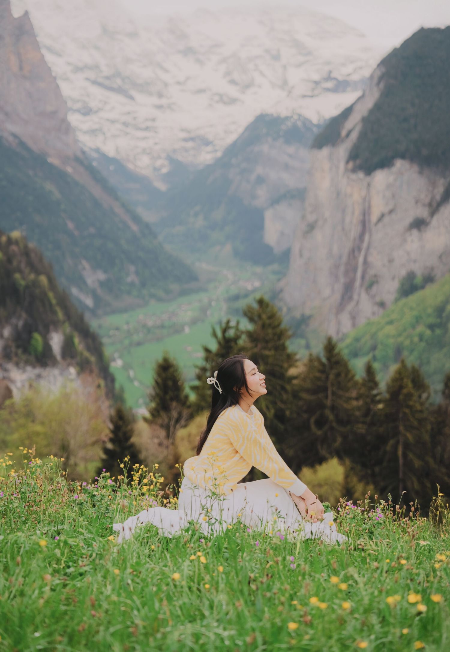 Woman in yellow sweater sitting peacefully in Swiss alpine meadow with Lauterbrunnen valley backdrop.