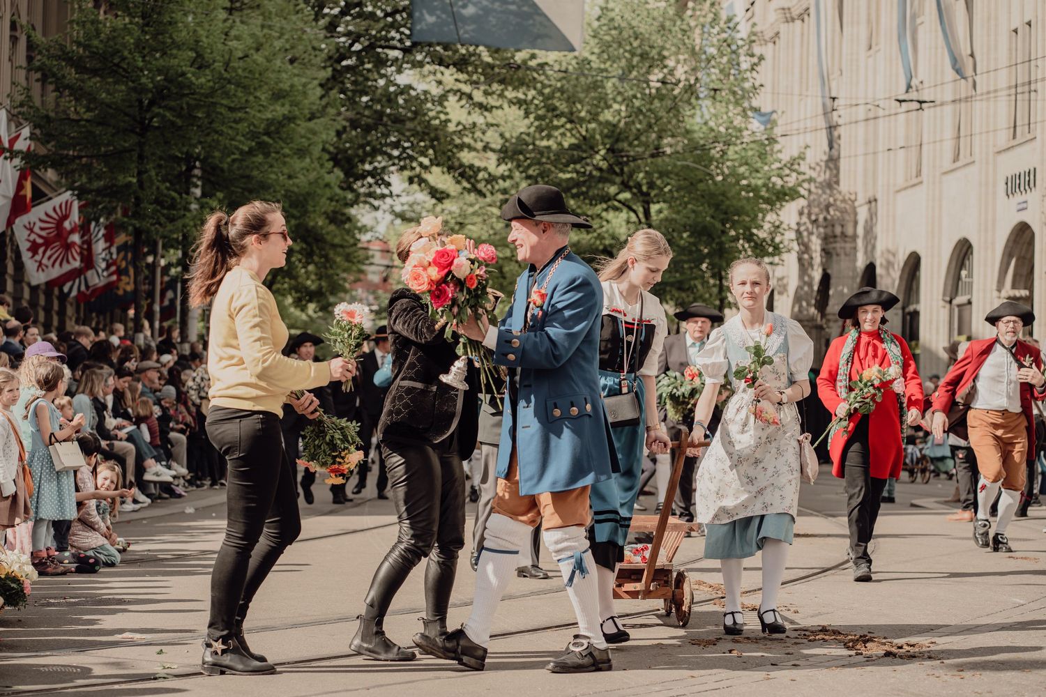 Performers in historical blue and red costumes distribute flowers to spectators at street parade.