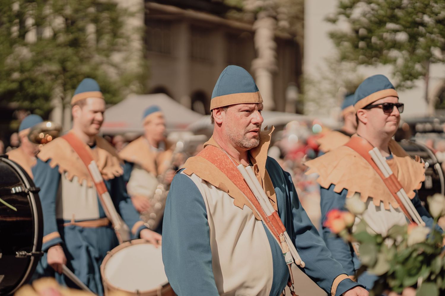Medieval parade performers in blue and gold costumes marching with drums at a traditional festival.