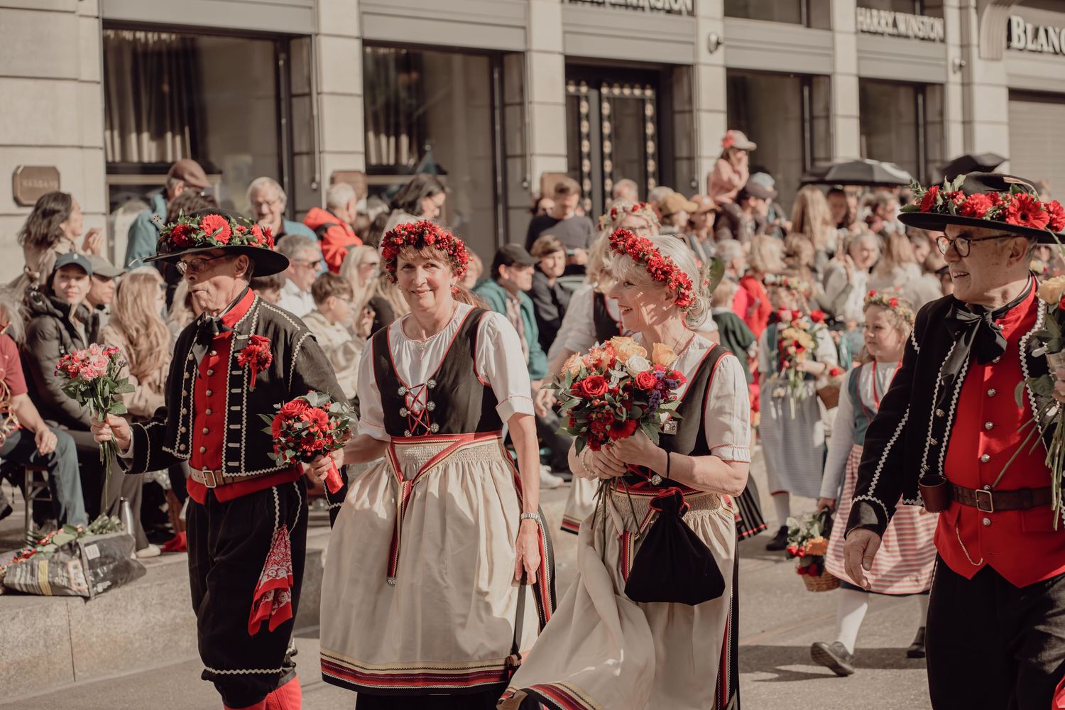 Participants in traditional Swiss folk costumes carry colorful flower bouquets during a festive cultural parade.
