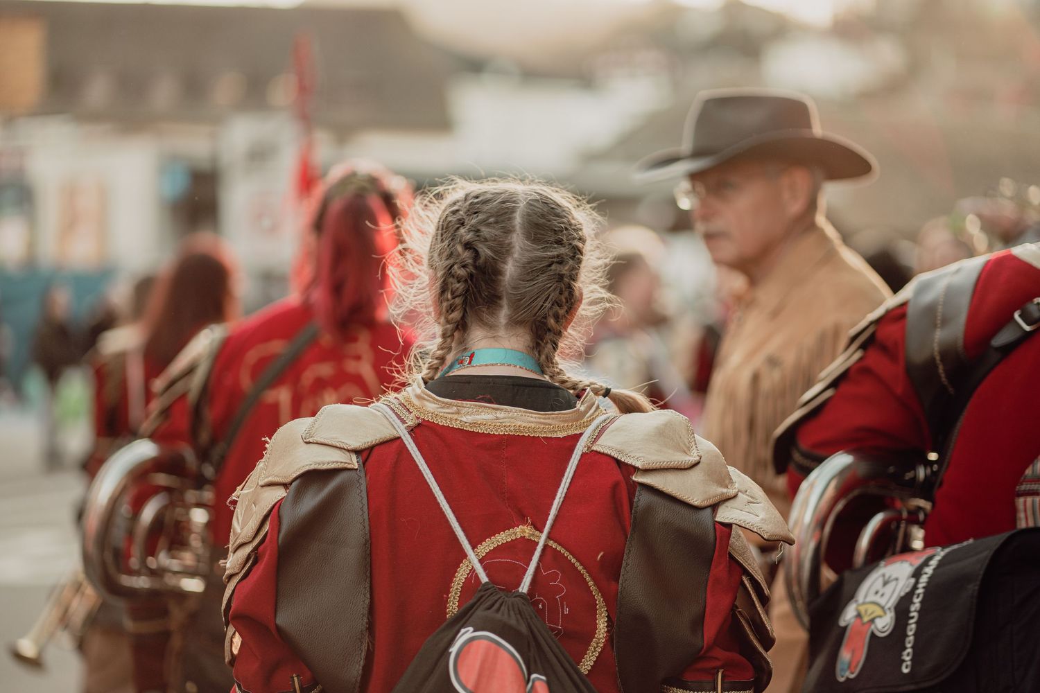 Young girl in red fantasy armor costume seen from behind at an outdoor festival event.