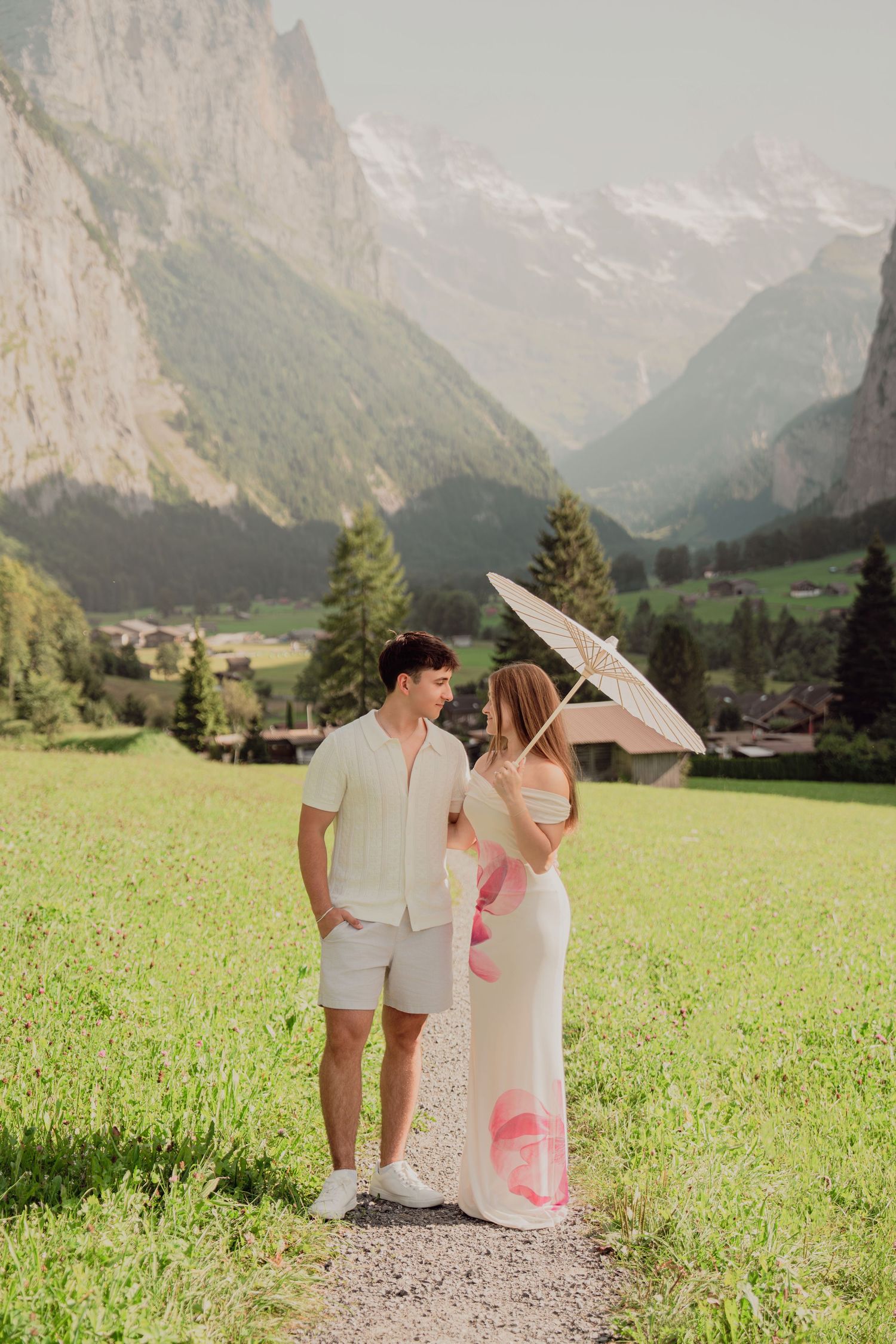 Romantic couple sharing a moment under white parasol in lush Lauterbrunnen valley with majestic Swiss Alps backdrop.