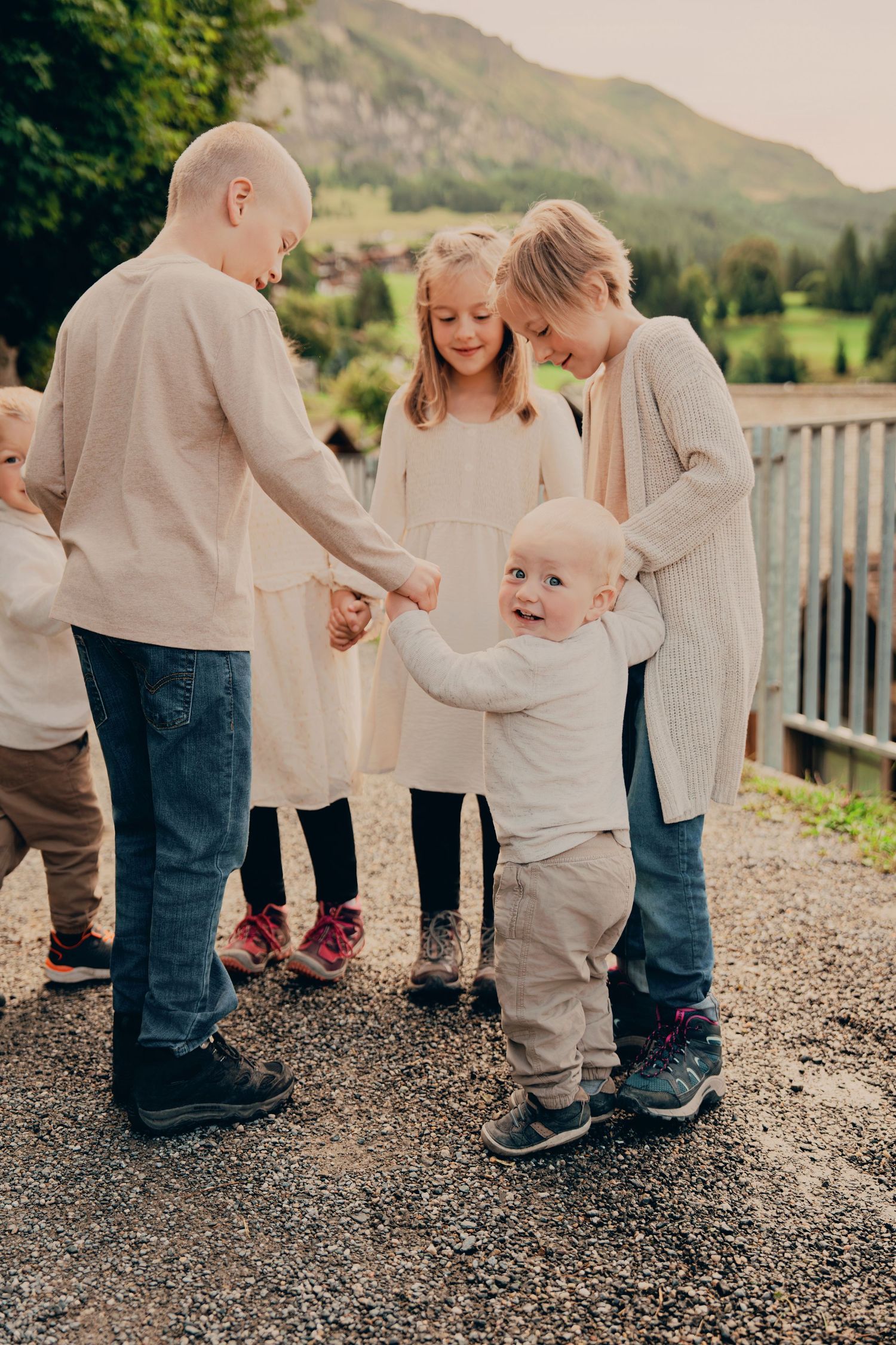 A toddler laughs joyfully while holding hands with older siblings on a mountain village path.