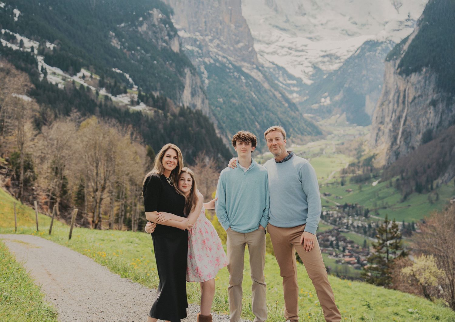 Family of four posing together on a hillside path with Swiss Alpine valley in background.