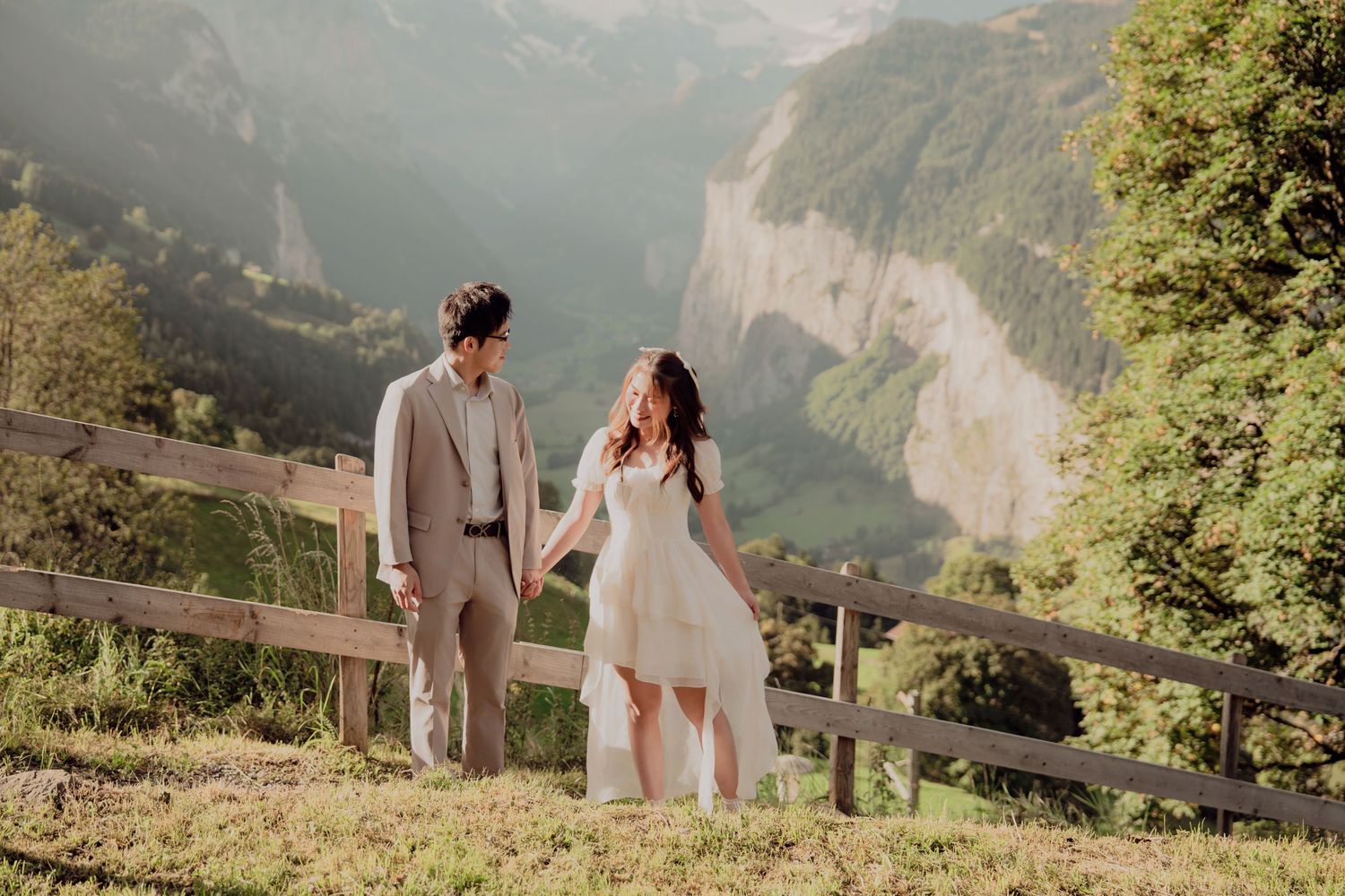 Wedding couple holds hands on a lush green hillside with stunning Lauterbrunnen valley cliffs in the background.