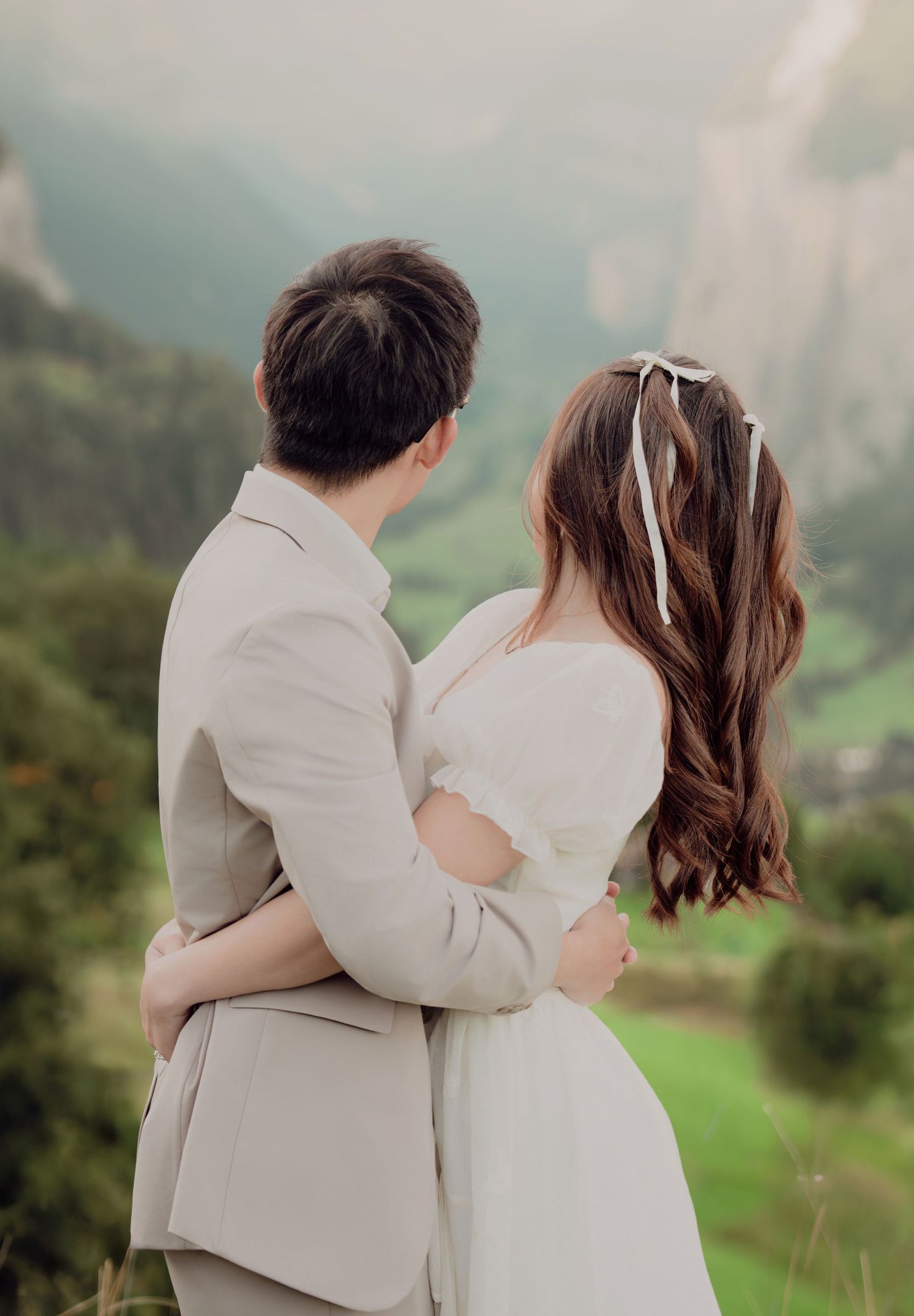Couple embracing from behind while gazing at a stunning misty mountain valley landscape together.