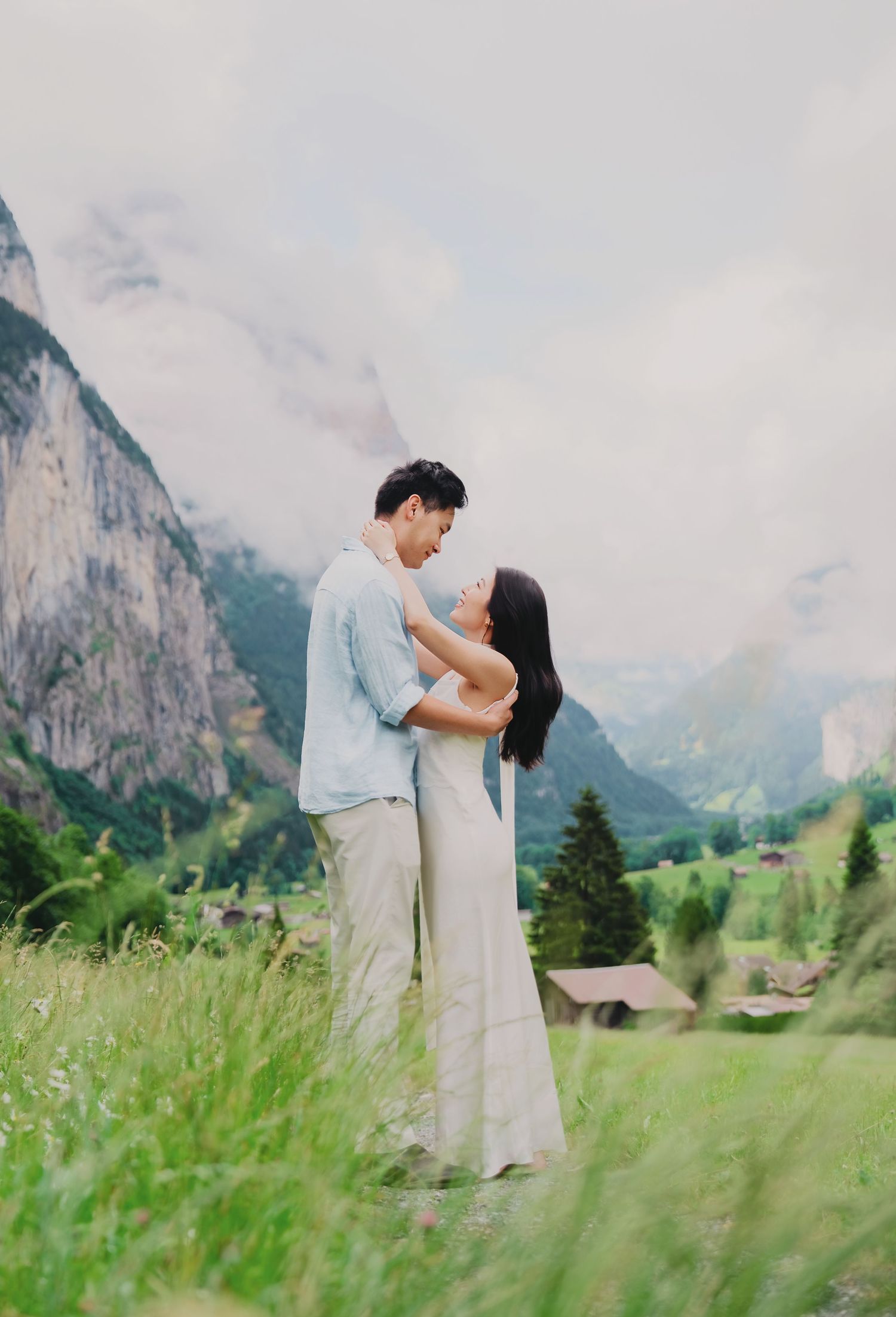 Couple embracing in a meadow with stunning misty mountain views in the Lauterbrunnen valley, Switzerland.