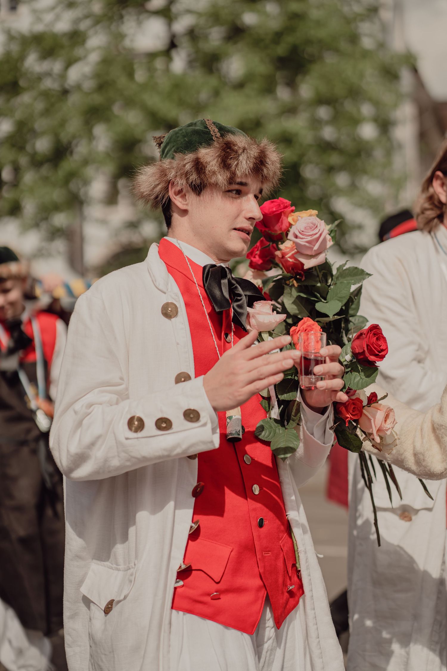 Young man in historical white and red costume holds a bouquet of roses at a parade.