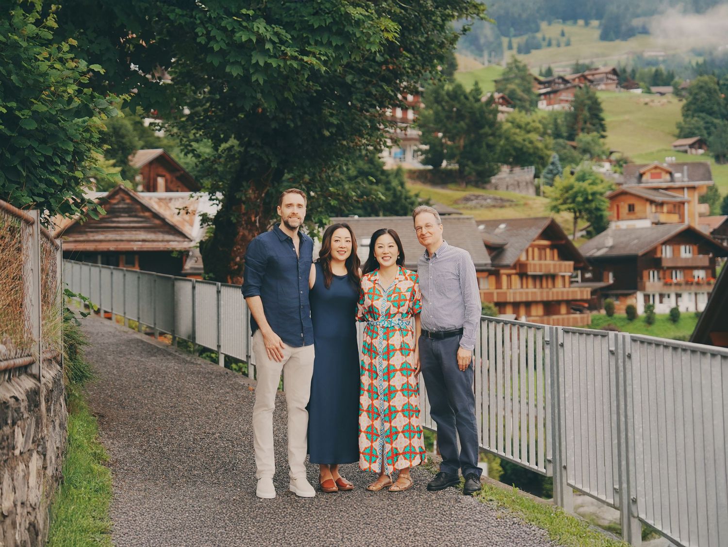 Two couples pose together on a scenic Swiss village pathway surrounded by lush green hills.