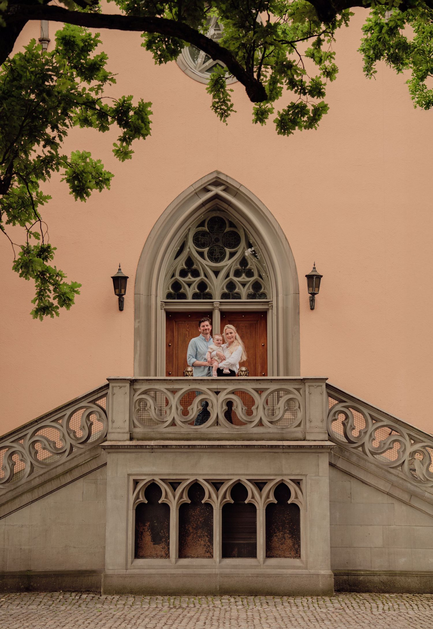 Family portrait on decorative Gothic church balcony framed by trees in Zurich.