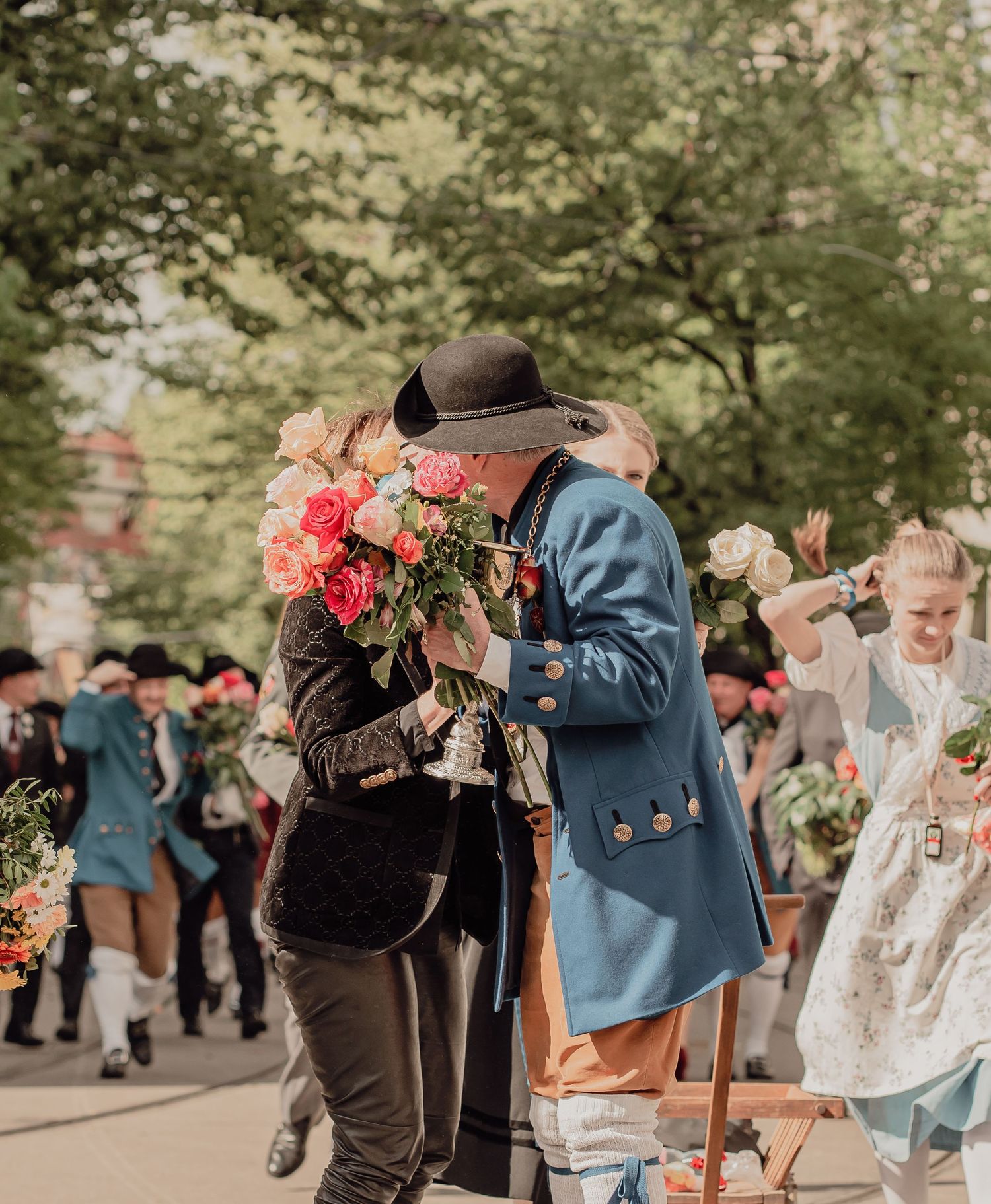 Person in blue historical costume presents colorful flower bouquet during outdoor festival parade.