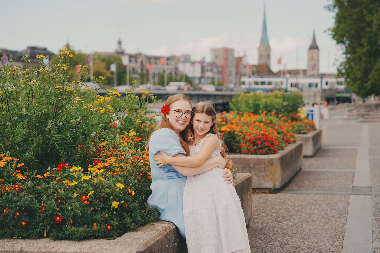 Two girls hugging warmly beside colorful flower beds along the Zurich lakeside promenade.