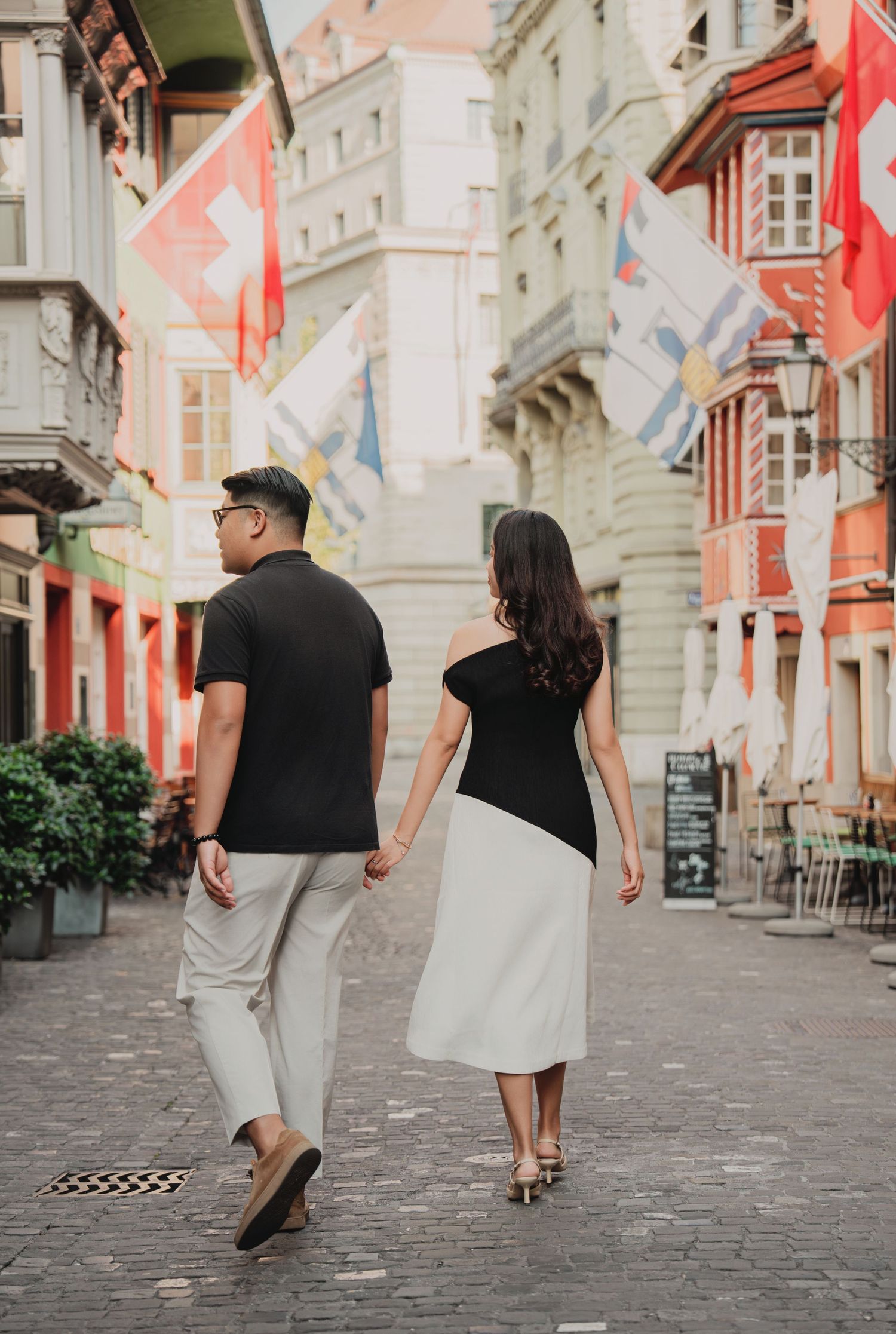 Couple walking away hand in hand along a Swiss street with Swiss flags and colorful historic buildings.