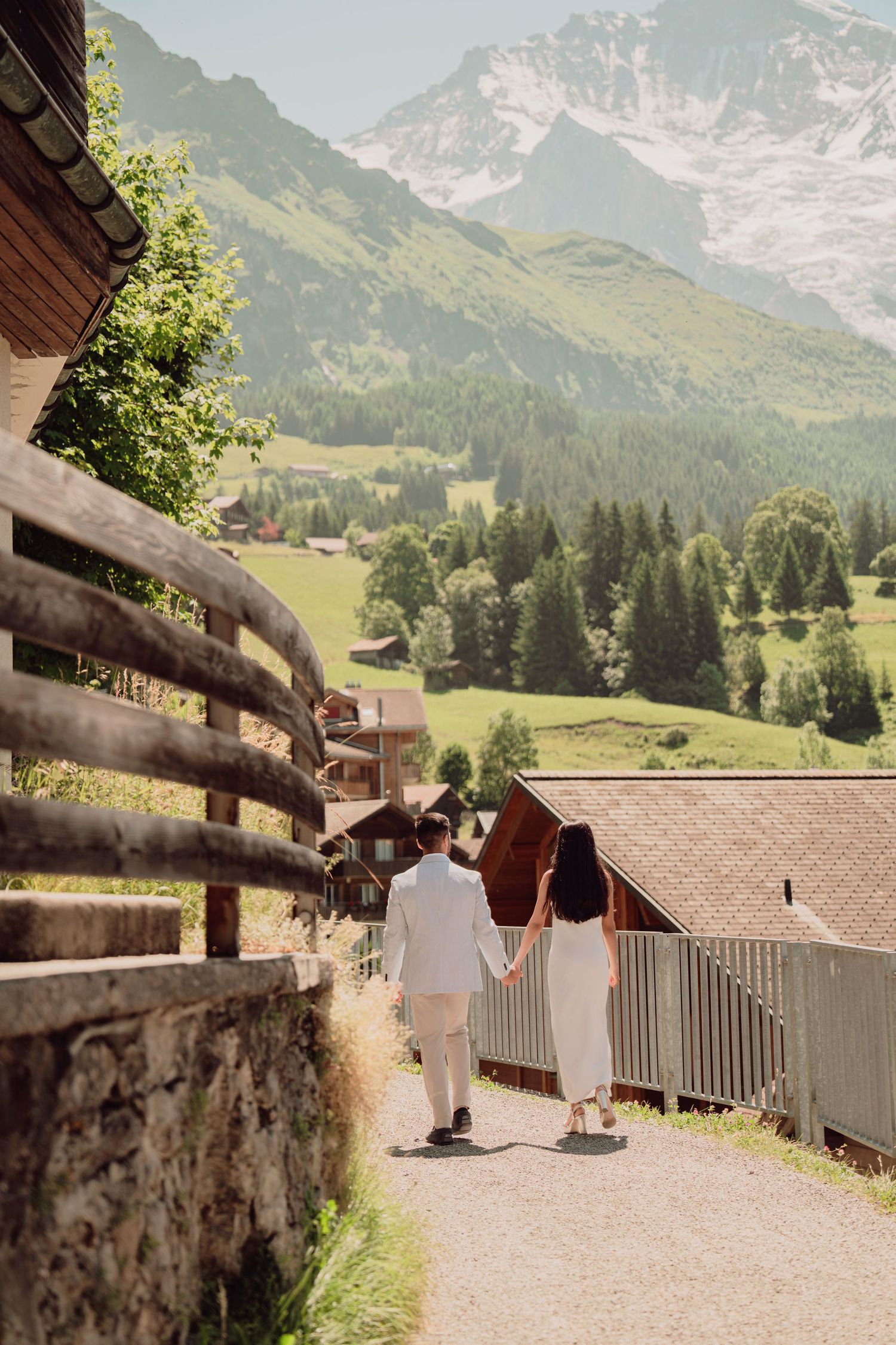 Couple holding hands walking along a scenic Alpine village path with mountain views in Switzerland.