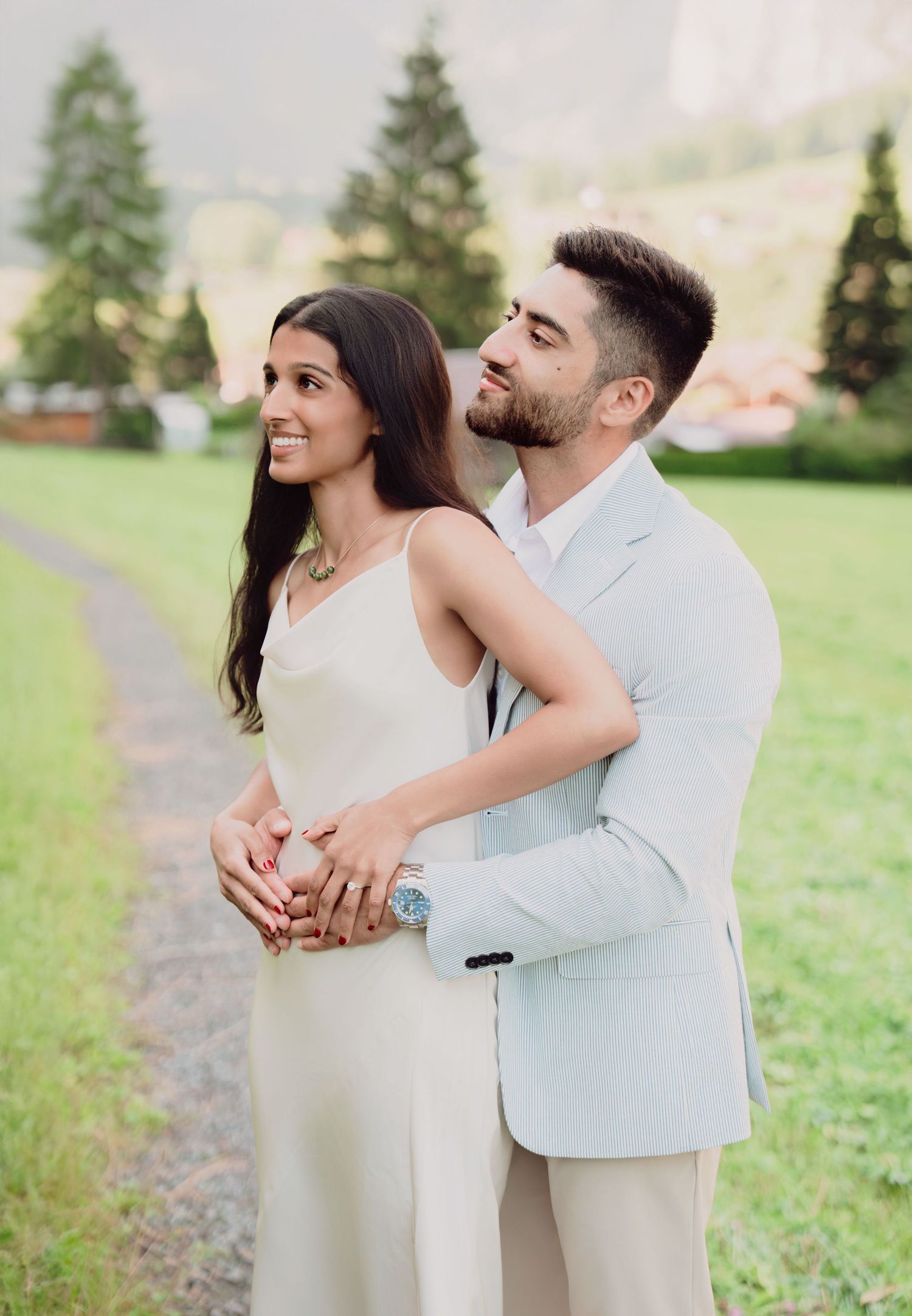 Groom embracing bride from behind as they gaze upward in a serene Alpine landscape.