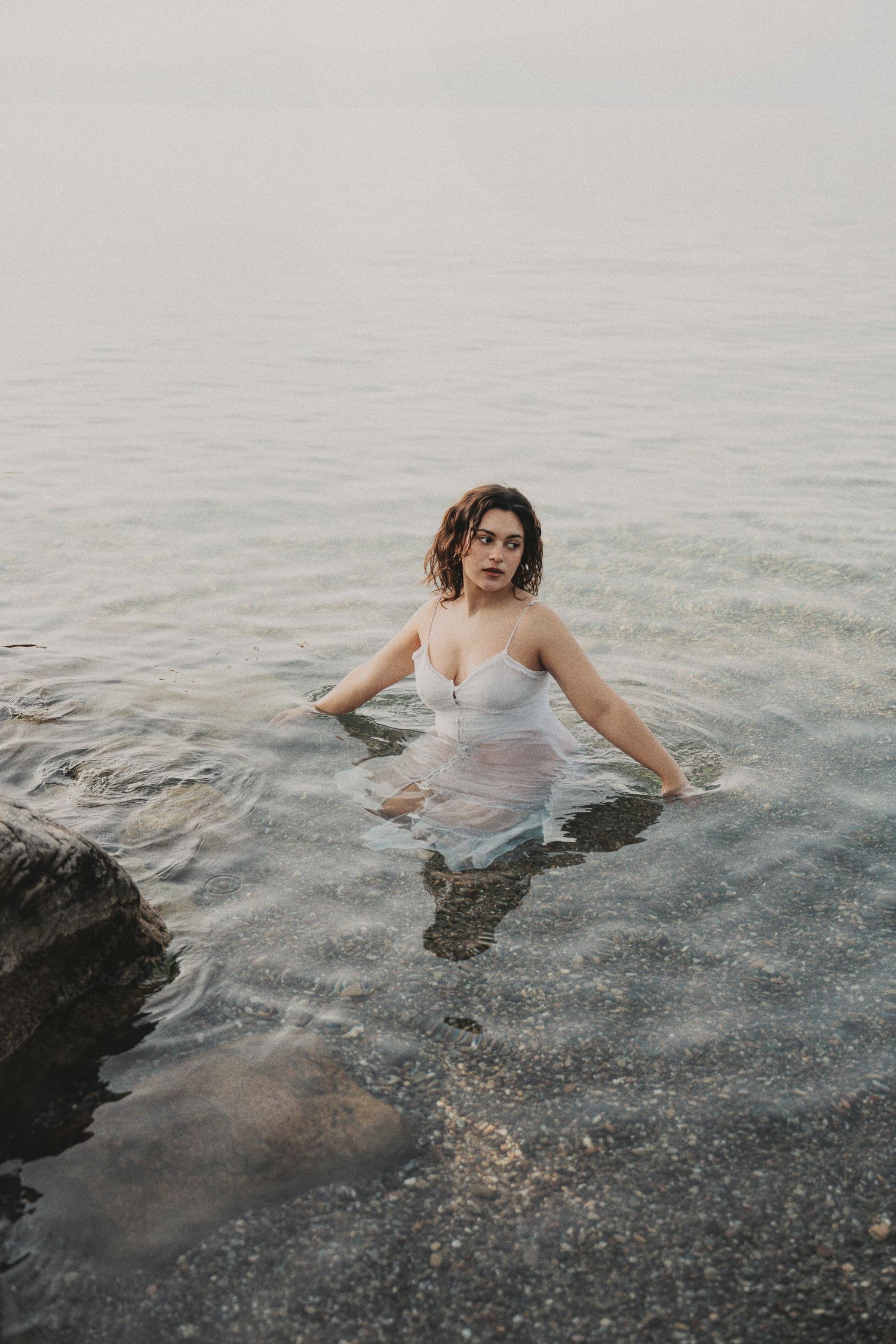 Woman in wet white dress sitting in calm ocean water.