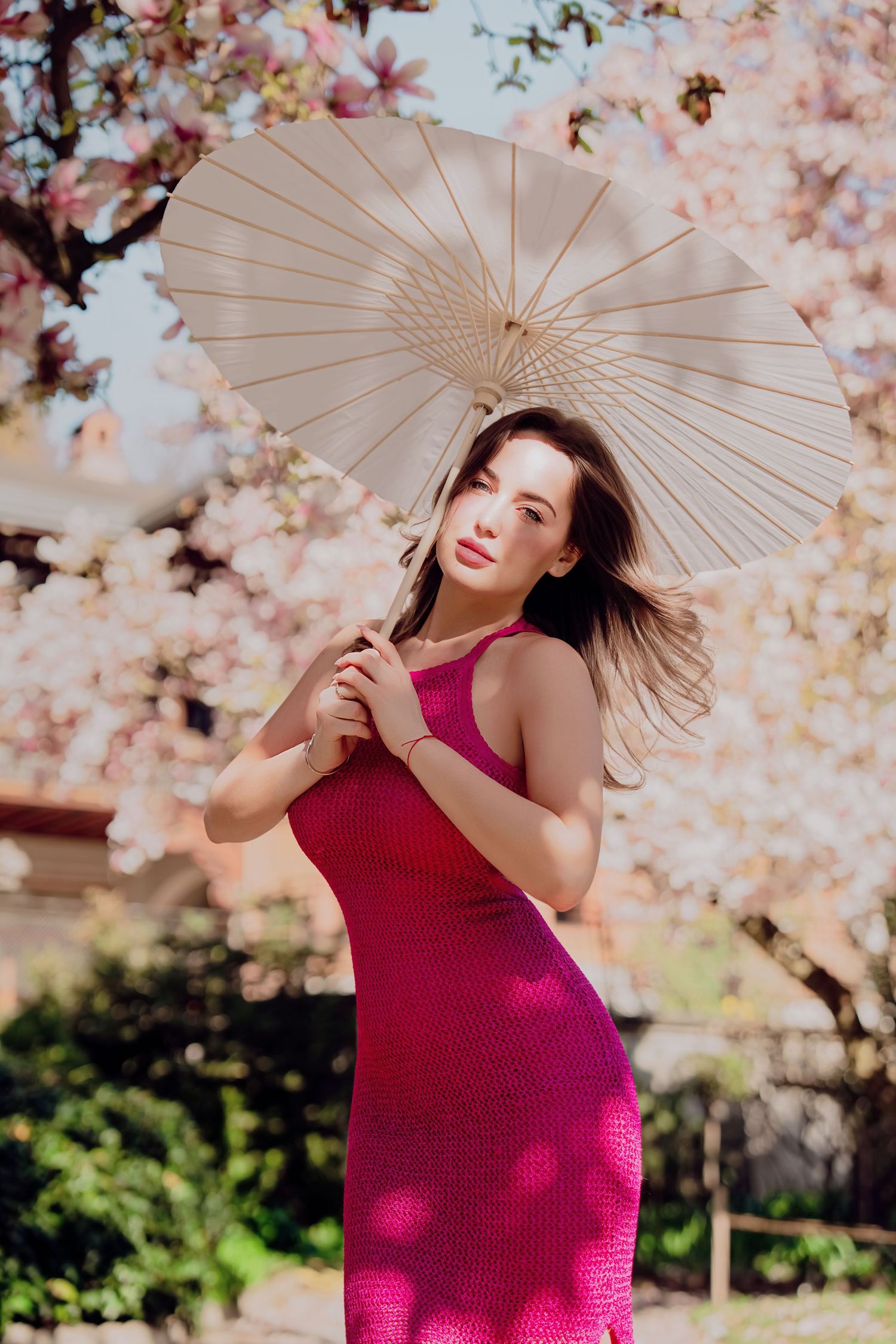 Woman in pink dress holding white parasol under blooming magnolia tree.