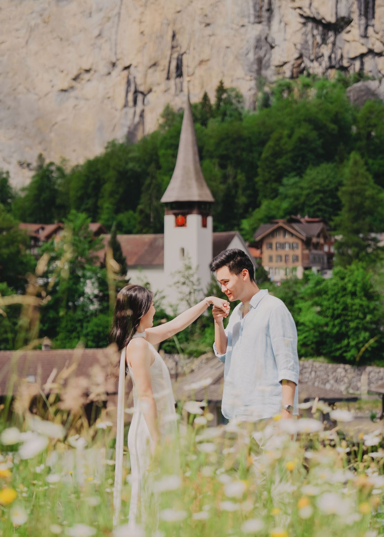 Romantic couple in a flower meadow with a charming Swiss church and cliffs in Lauterbrunnen, Switzerland.