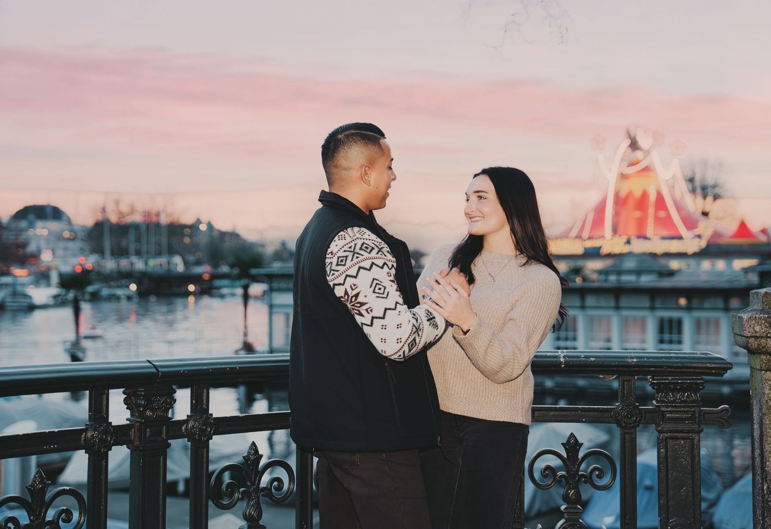 Romantic couple holding hands on ornate bridge at sunset with Zurich Christmas market behind.