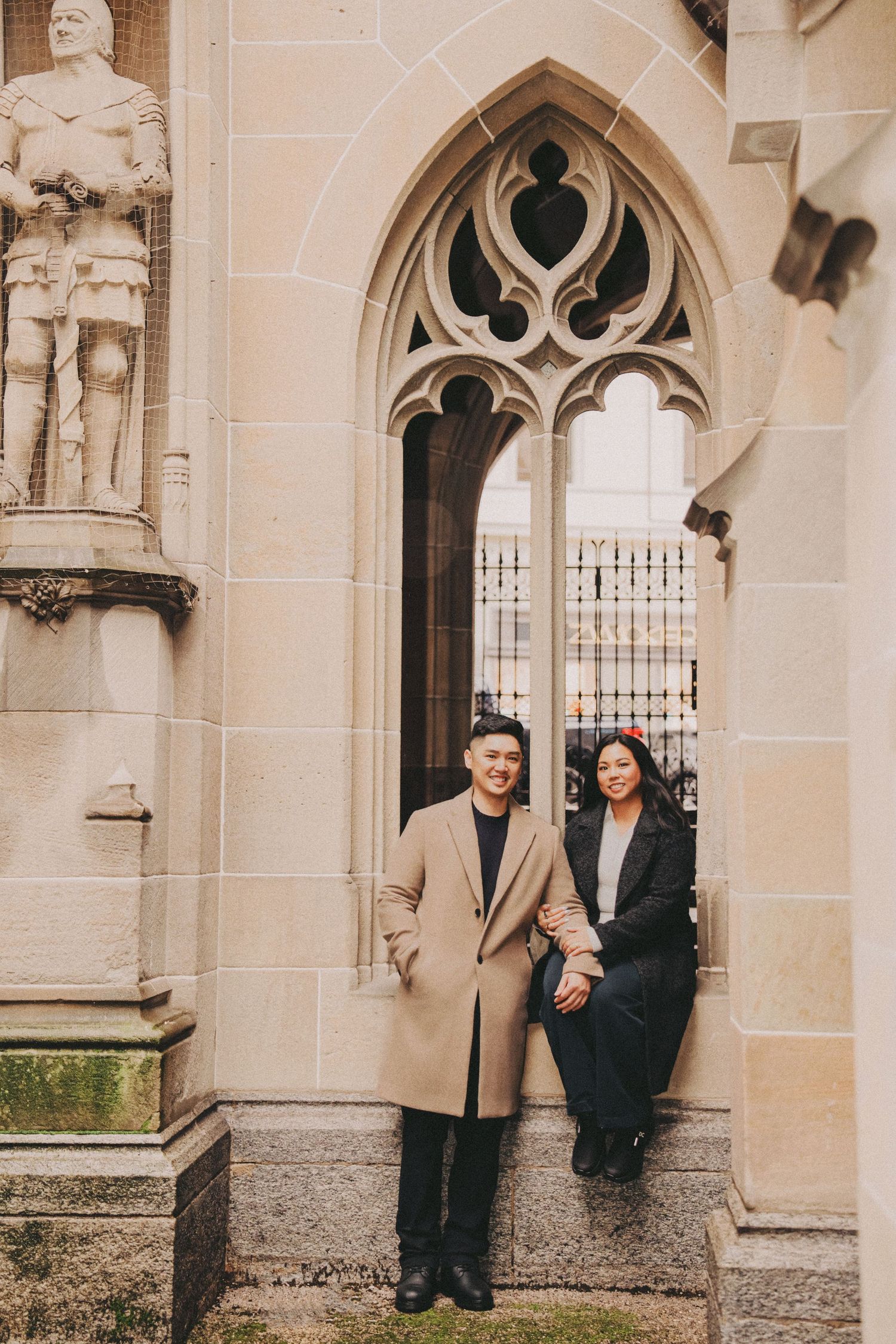 Couple posing by gothic stone archway with medieval knight statue.